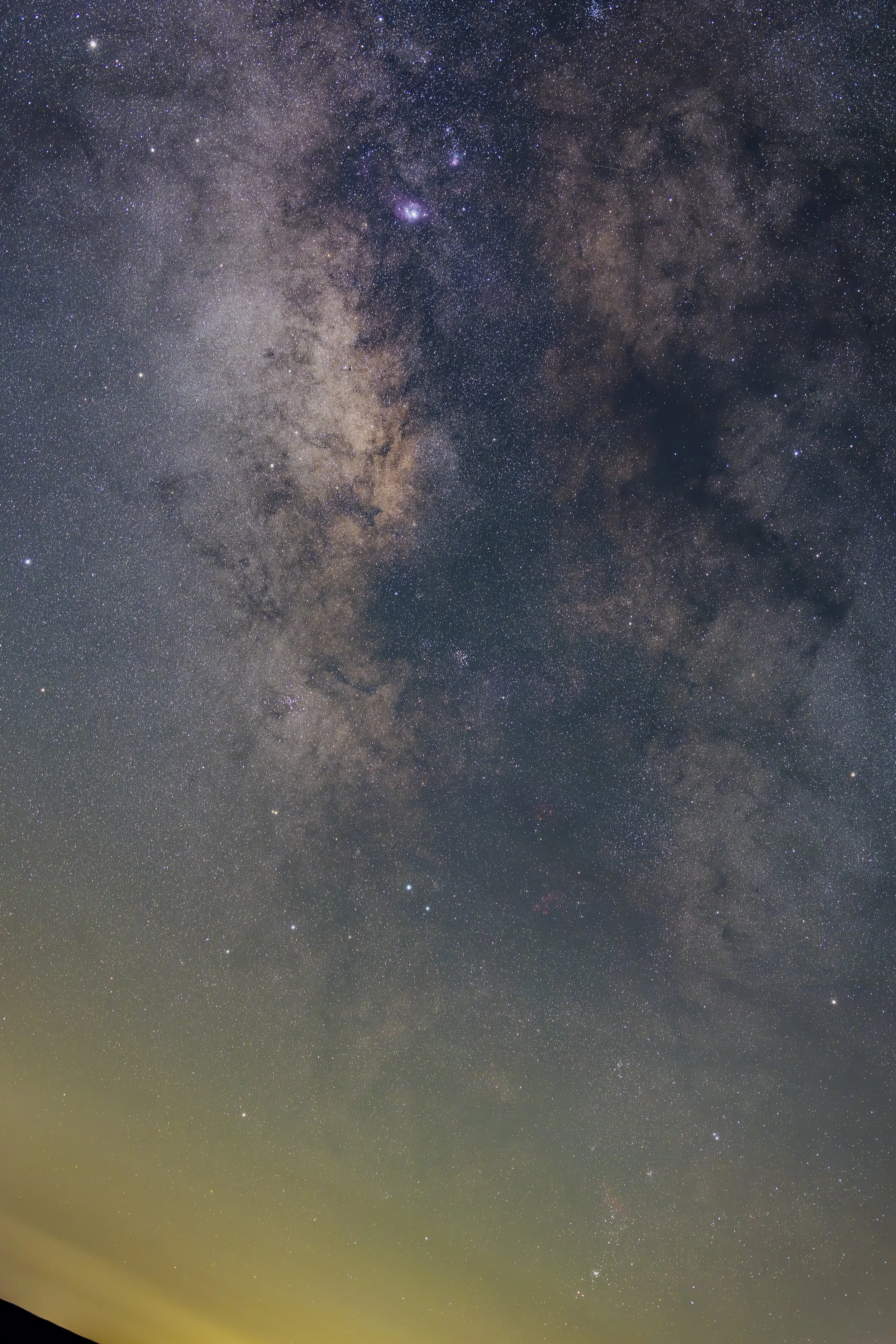 Photograph of the night sky showing the Milky Way galaxy with numerous stars and cosmic dust, some faint clouds near the horizon.