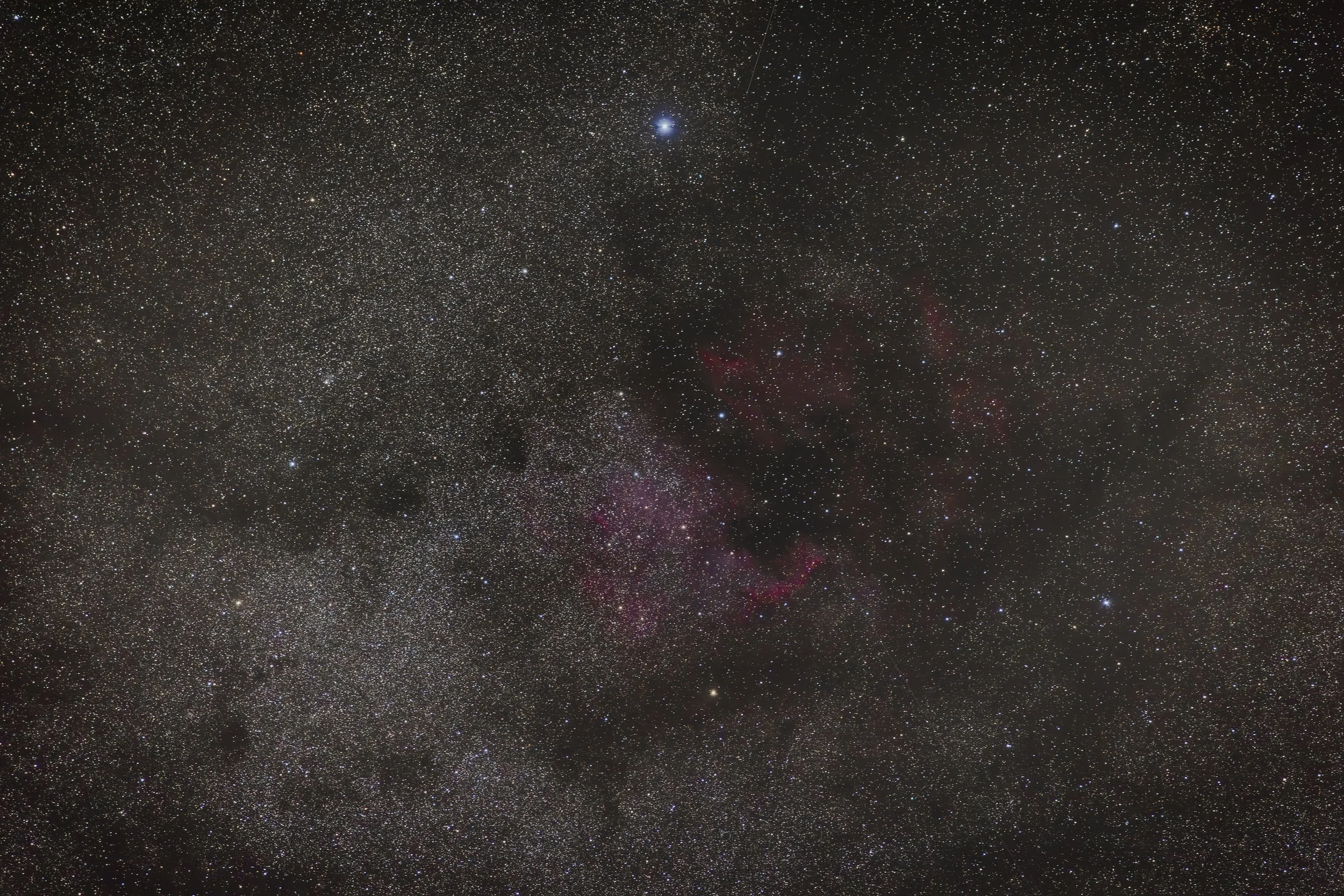 View of outer space filled with countless stars, nebulae, and a faint shooting star.