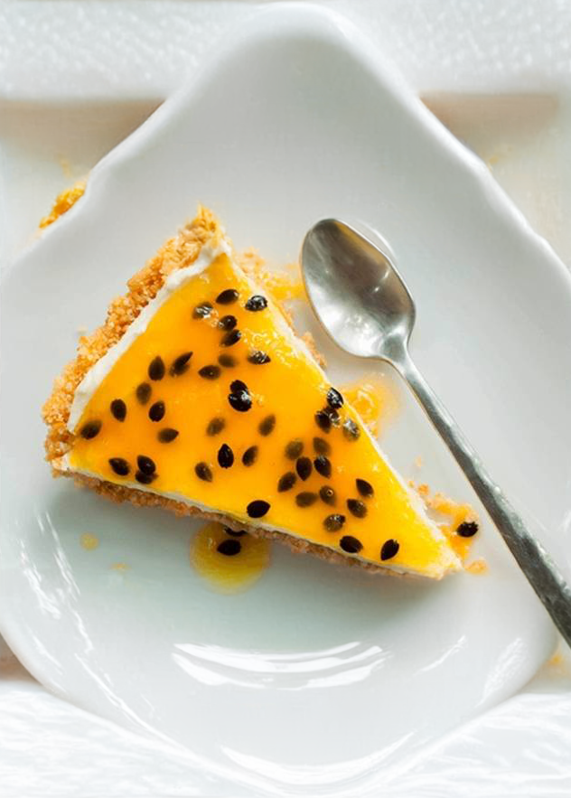 Slice of passion fruit cheesecake with yellow topping and black seeds on a white plate with a spoon