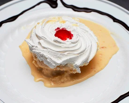 Dessert with whipped cream, a red cherry, yellow sauce, and chocolate drizzle on a white plate.