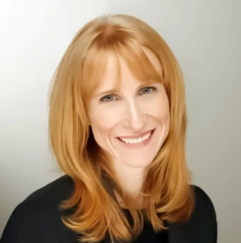 Woman with long red hair smiling at the camera, wearing a black top against a light background.