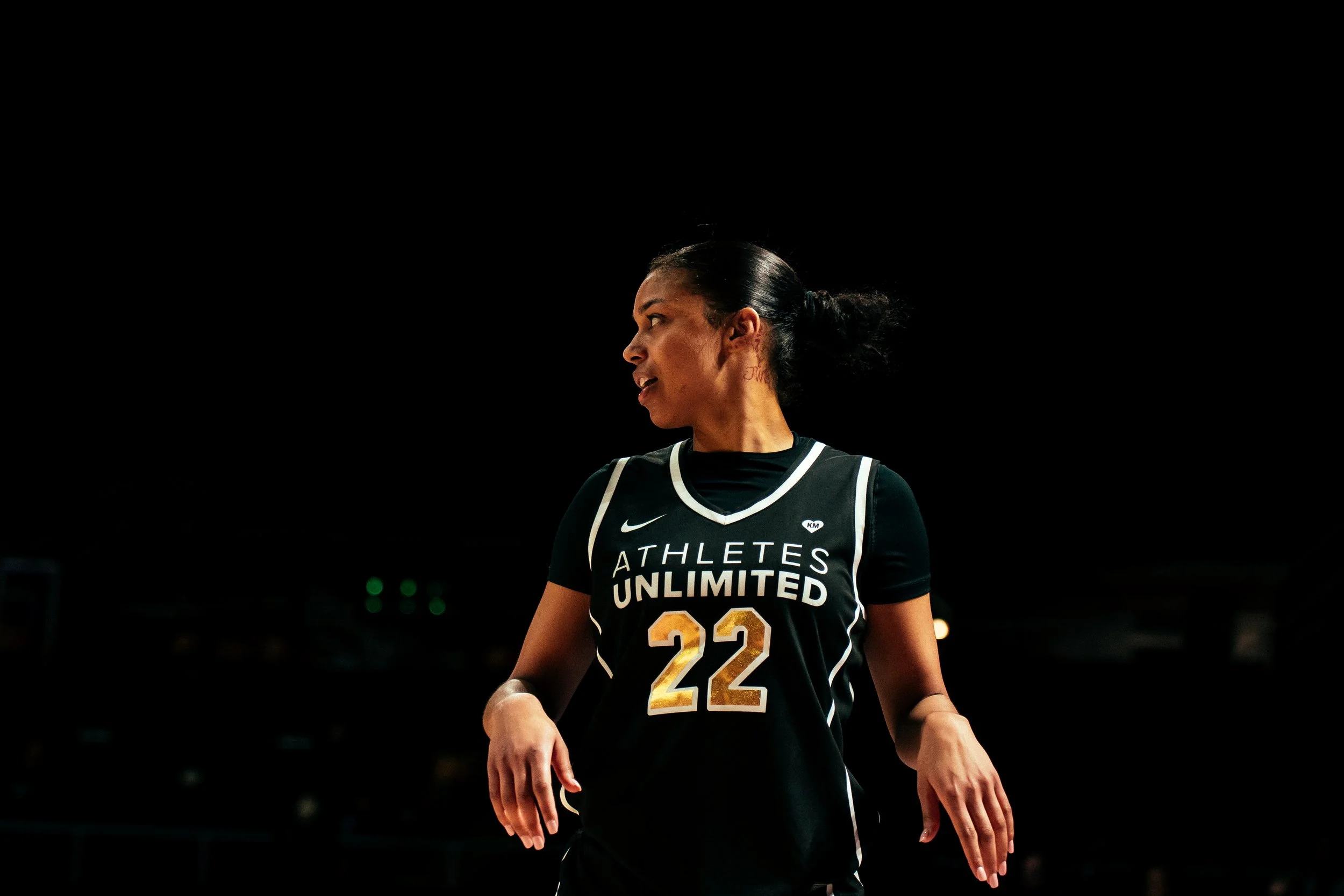 Female basketball player wearing a black jersey with the number 22 and the words 'Athletes Unlimited' on it, standing on the basketball court.