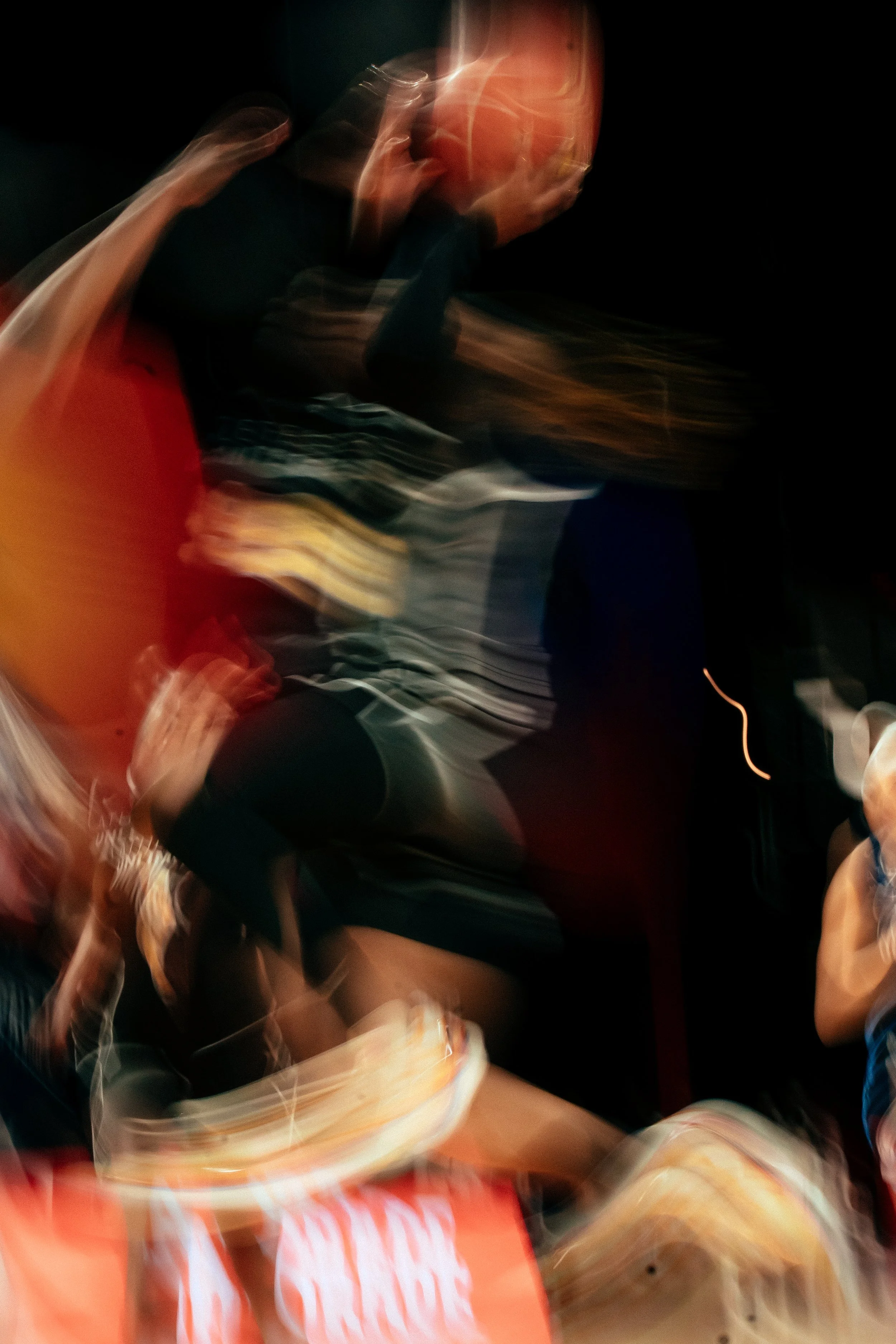 Blurry image of a person with a bald head wearing a dark shirt, sitting on a chair and talking on the phone in a dark environment.