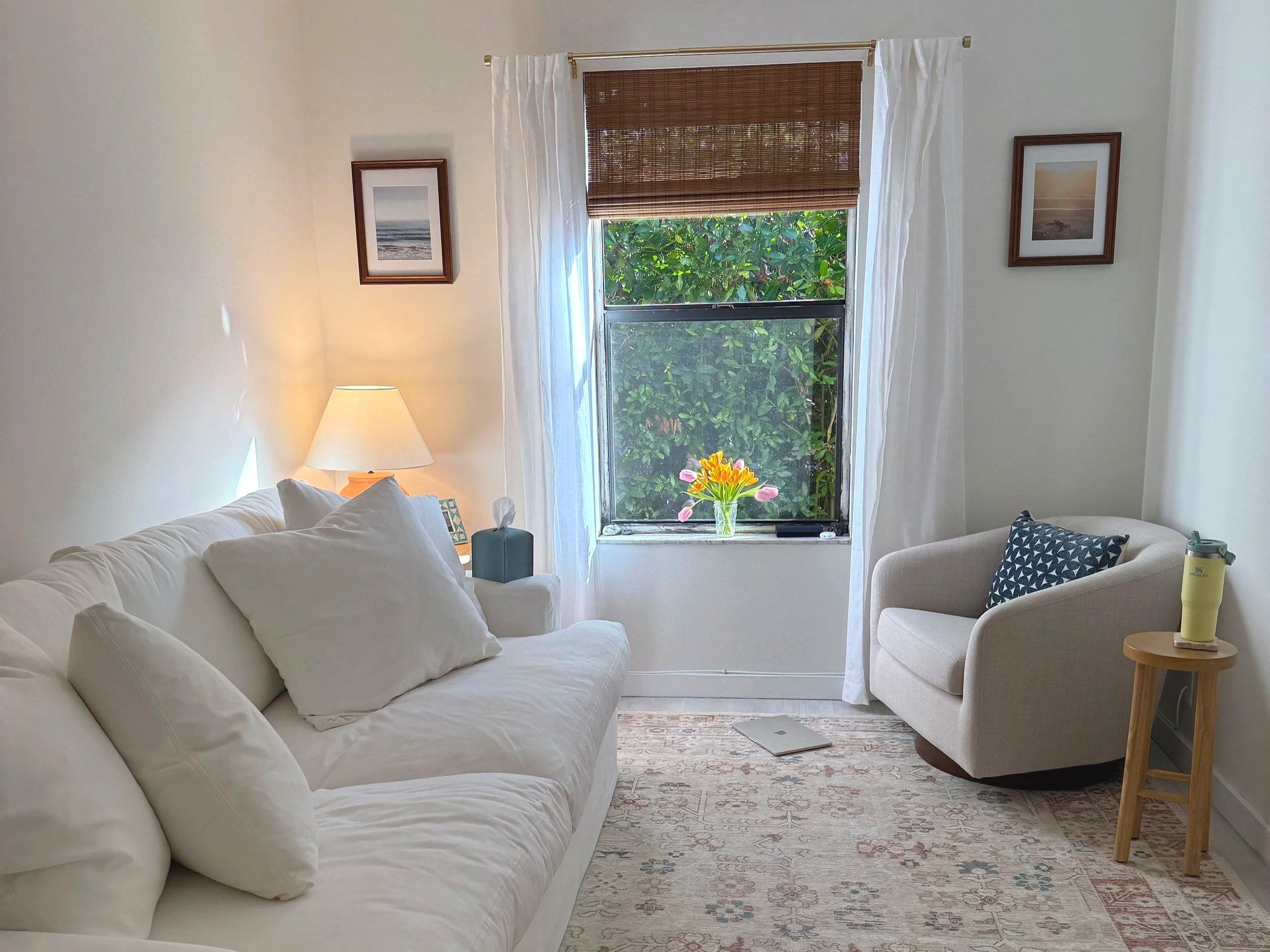 Stacked rocks balanced on a piece of driftwood on a sandy beach with ocean waves and a cloudy sky in the background.