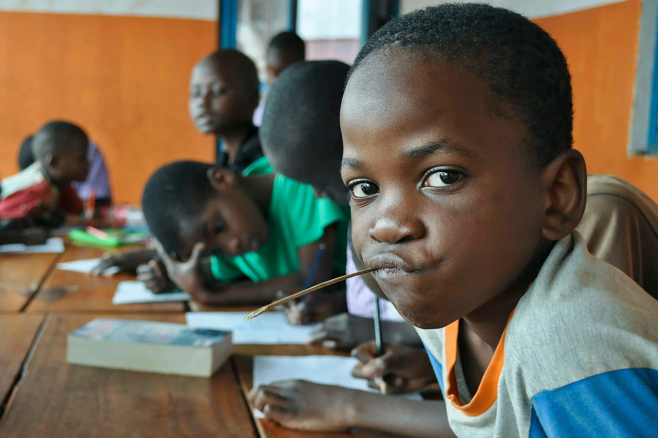 A child loonking into the camera and others reading and writing