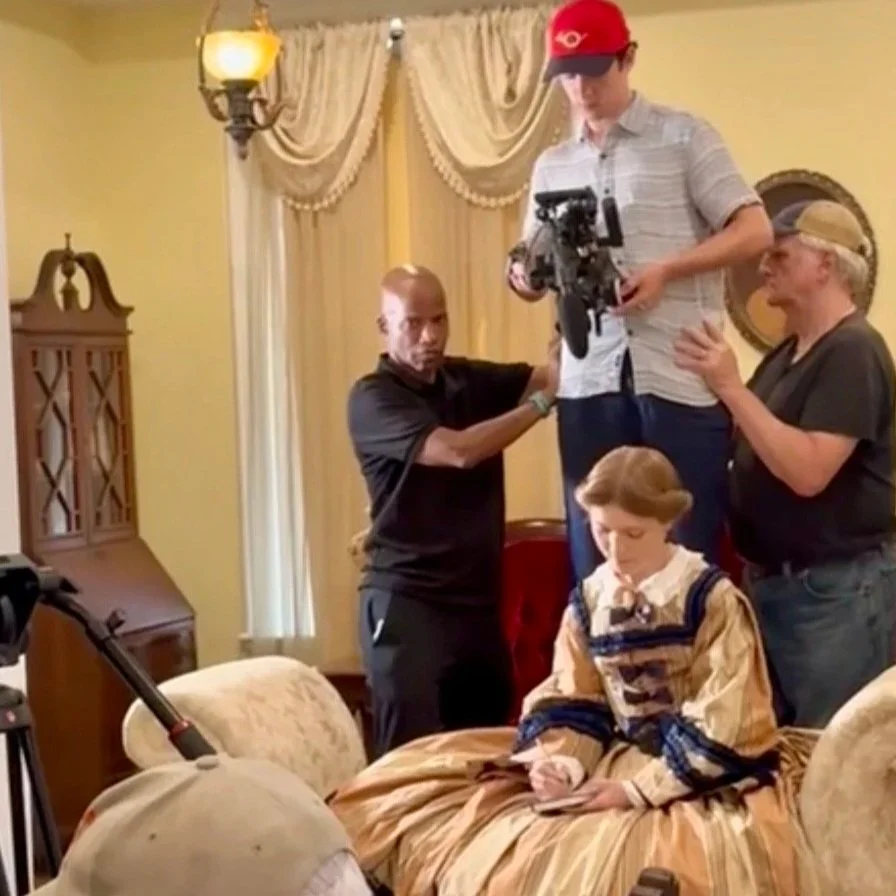 "Making the Film" --  

Brad Graham & George Edwards steady Jacob L.T. Bates while he is holding a camera and filming, standing on a makeshift riser.