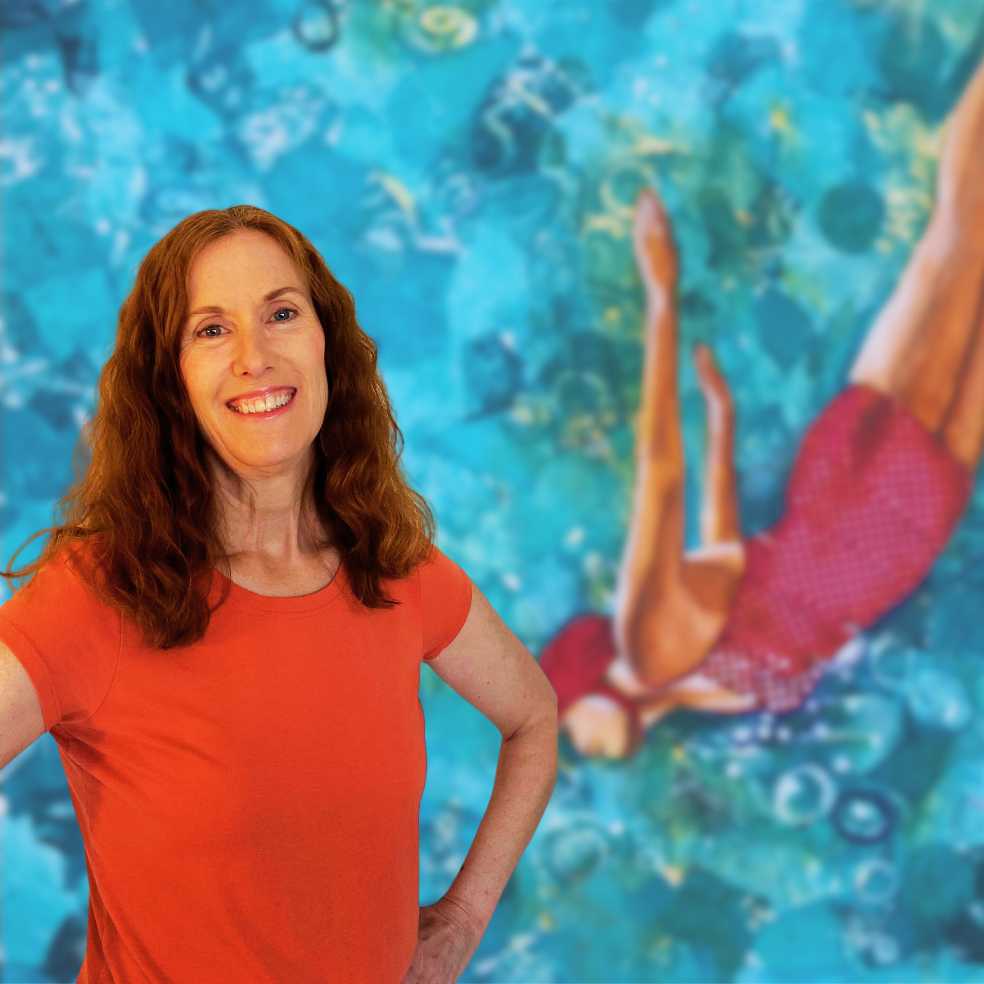 Smiling woman in an orange shirt standing in front of a colorful abstract painting of a swimmer in water.