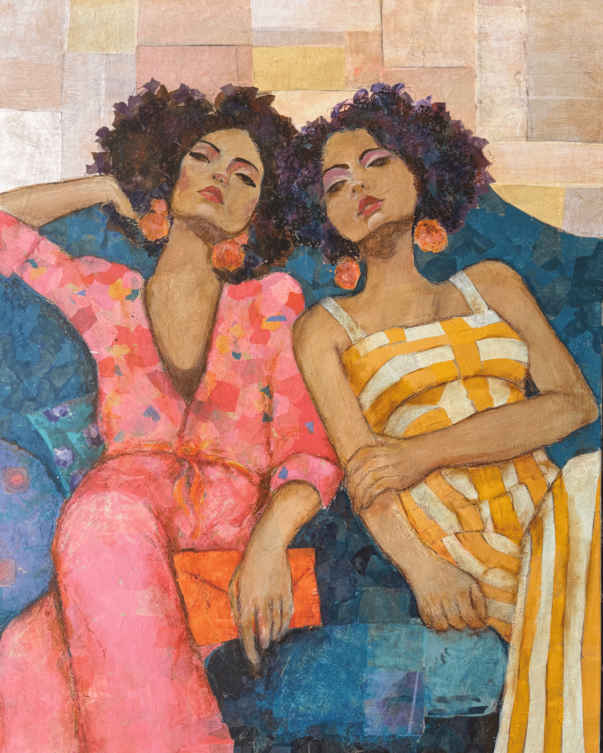 two women lounge together on a blue sofa looking pleasantly tired pink floral jumpsuit and yellow and white jumpsuit