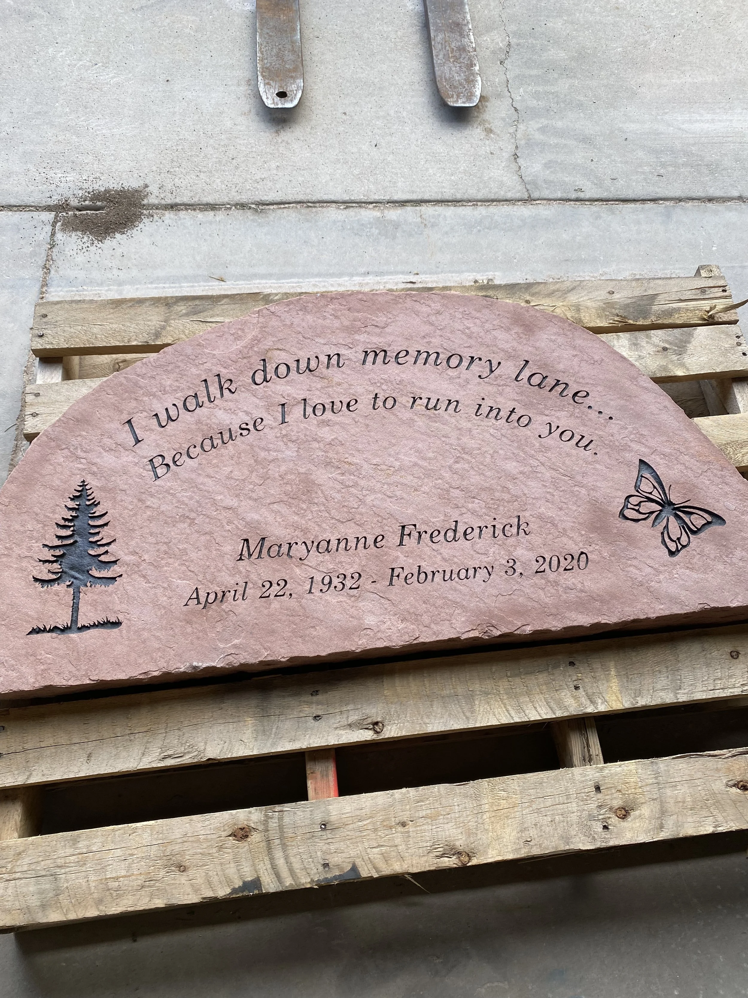 Stone memorial plaque with text and engravings, resting on a wooden pallet