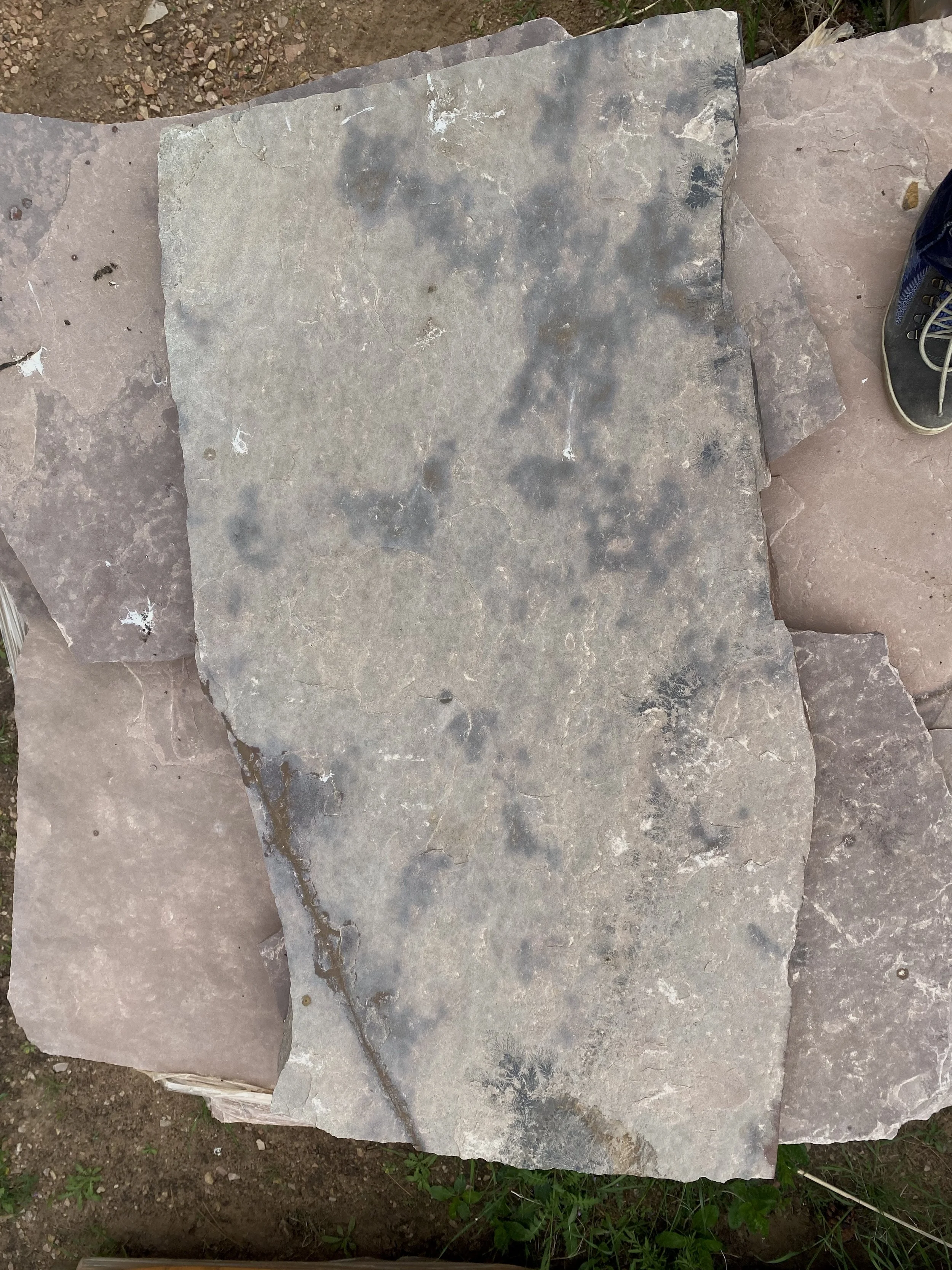 A large, flat stone with a rough surface and irregular edges, placed on other similar stones outdoors on dirt and grass.