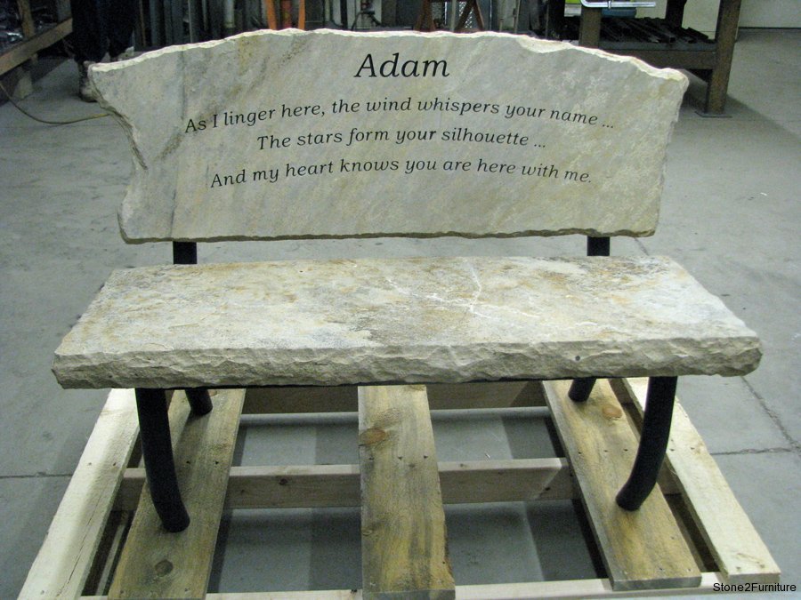 Stone memorial bench with engraved text, with backrest inscription for someone named Adam, and poetic phrases about wind, stars, and heart.