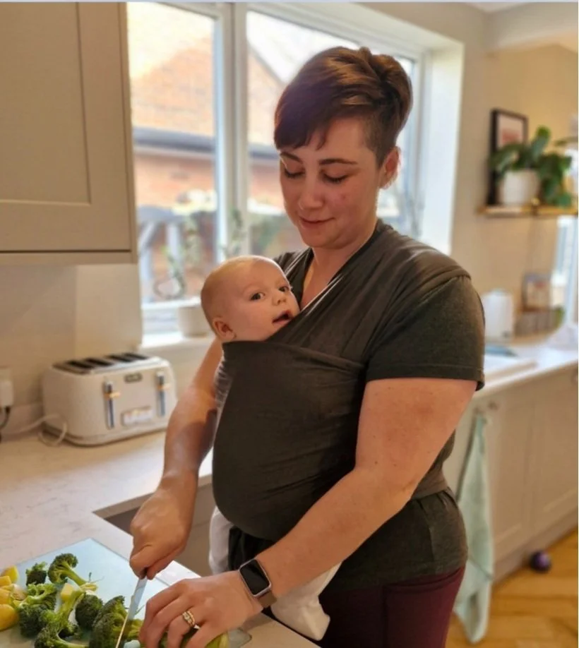 Doula preparing food while carrying a baby in a sling.