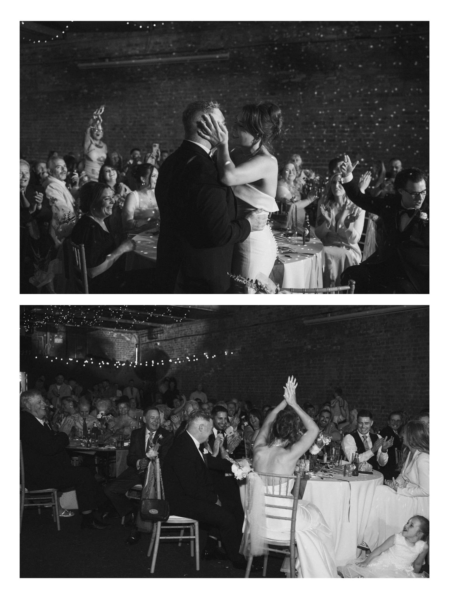 Indoor wedding reception where a bride and groom are dancing closely together in the center, with guests sitting and cheering around them, some clapping and smiling, under string lights on a brick wall.