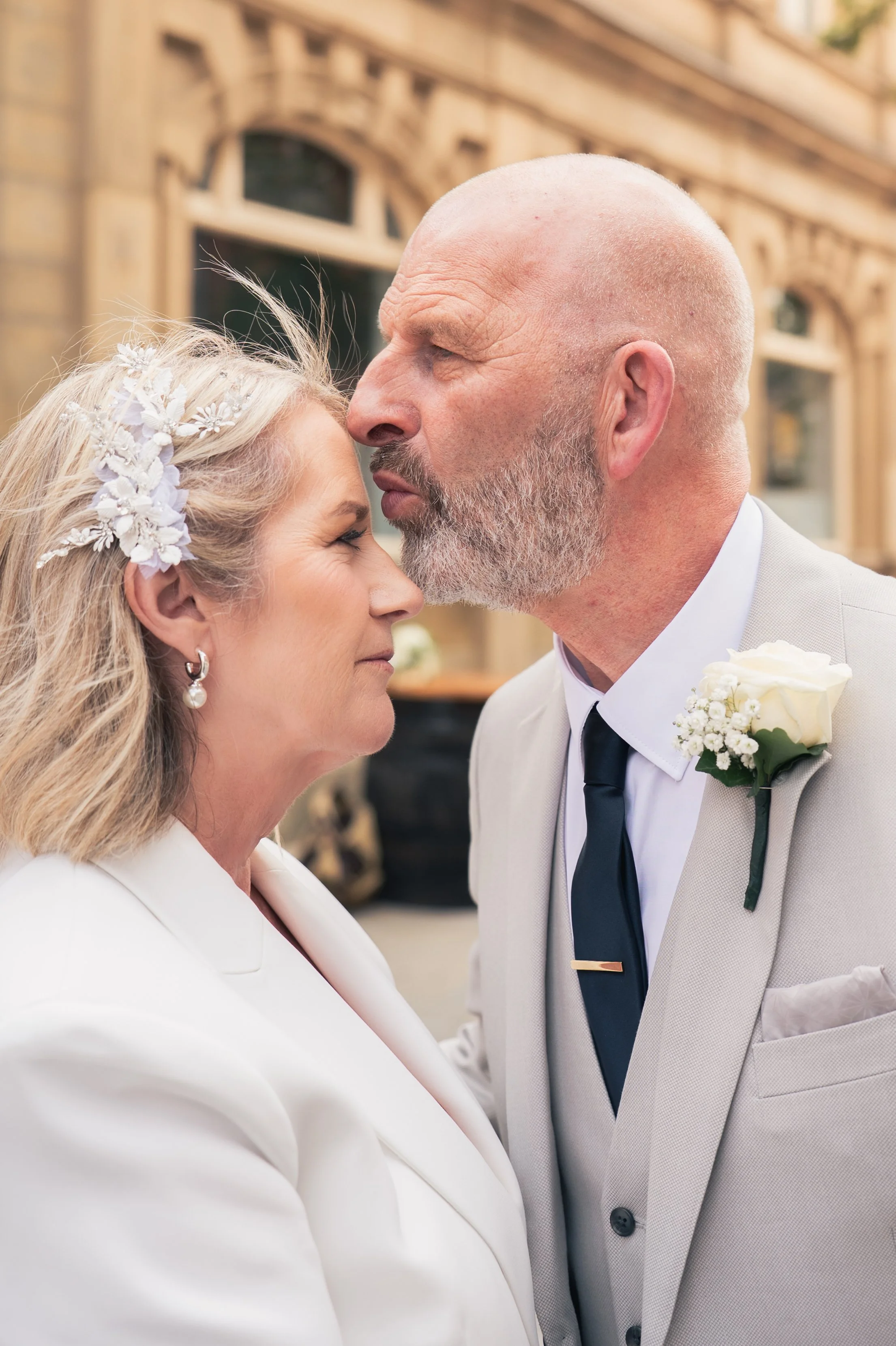 A couple, dressed in wedding attire, touching foreheads during a wedding ceremony outdoors.