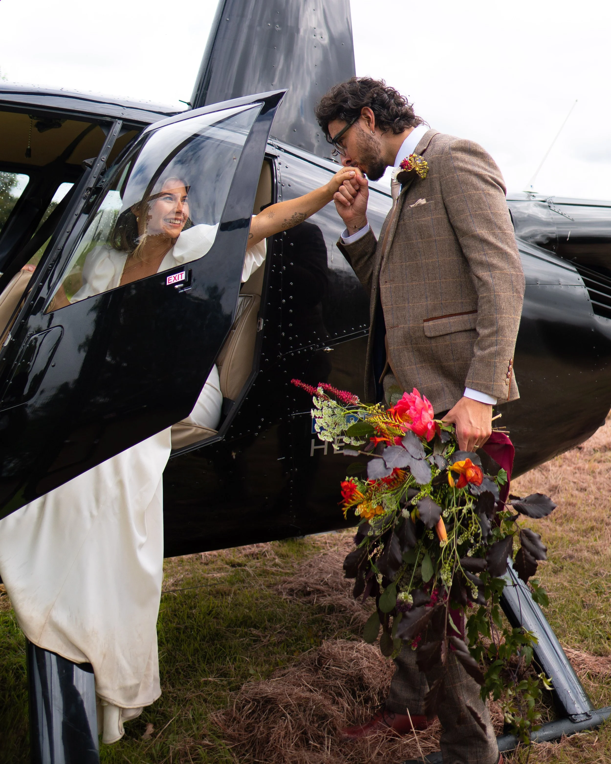 Bride exiting helicopter, groom holding flowers and kissing her hand