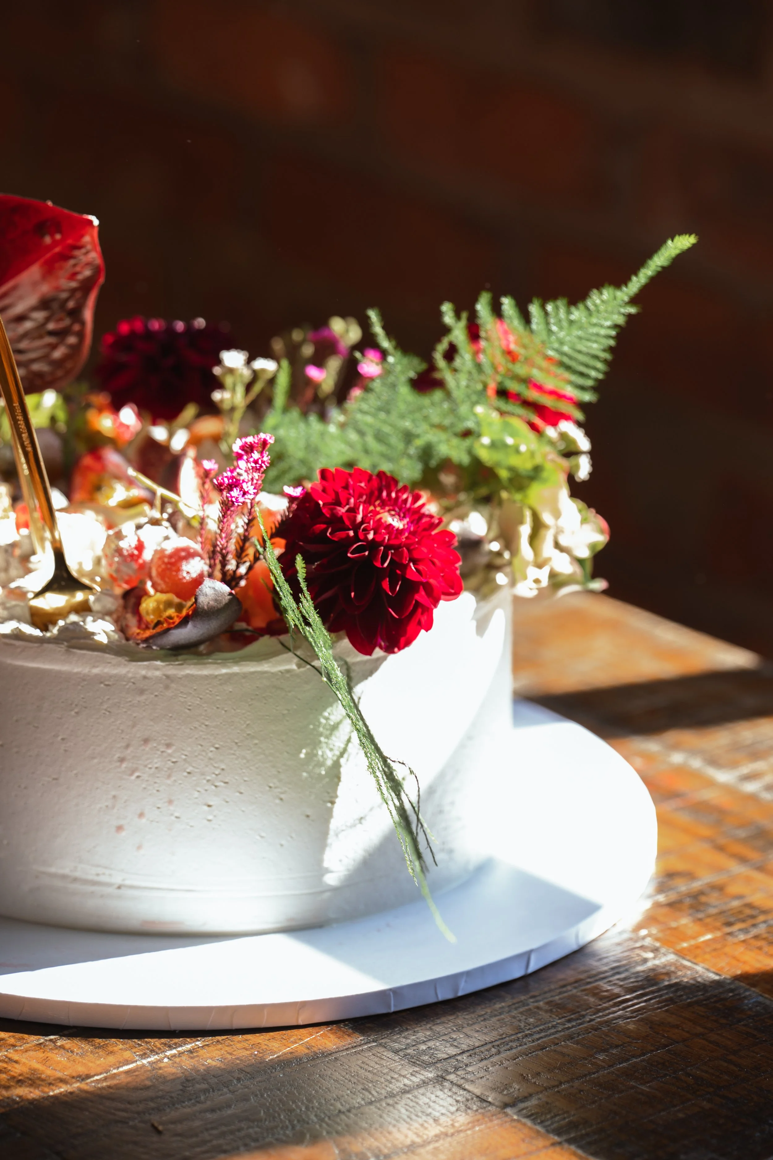 Close-up of a white frosted cake decorated with red flowers and greenery, placed on a wooden table.