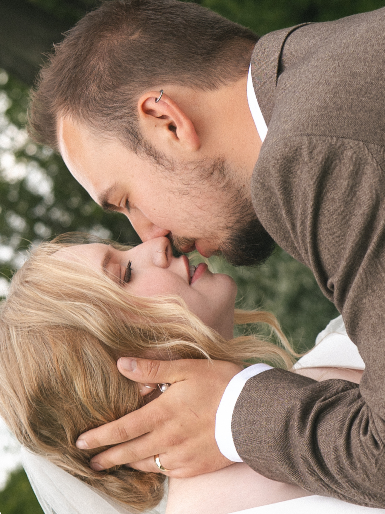 A couple kissing outdoors, with the woman holding the man's face and the man holding the woman's head, both with eyes closed.