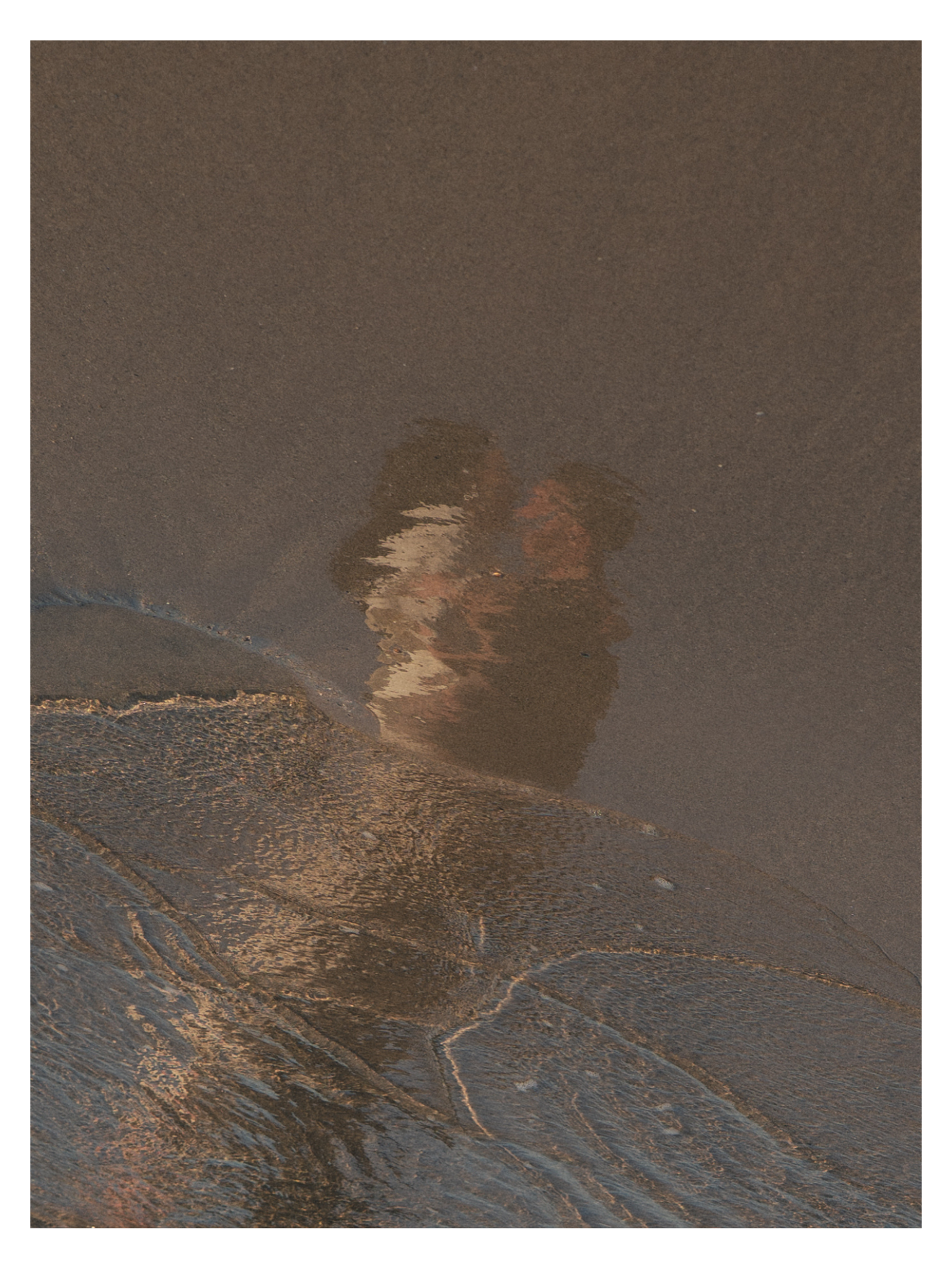 Reflected image of a woman with curly hair taking a photo on the beach at sunset, showing waves and sand