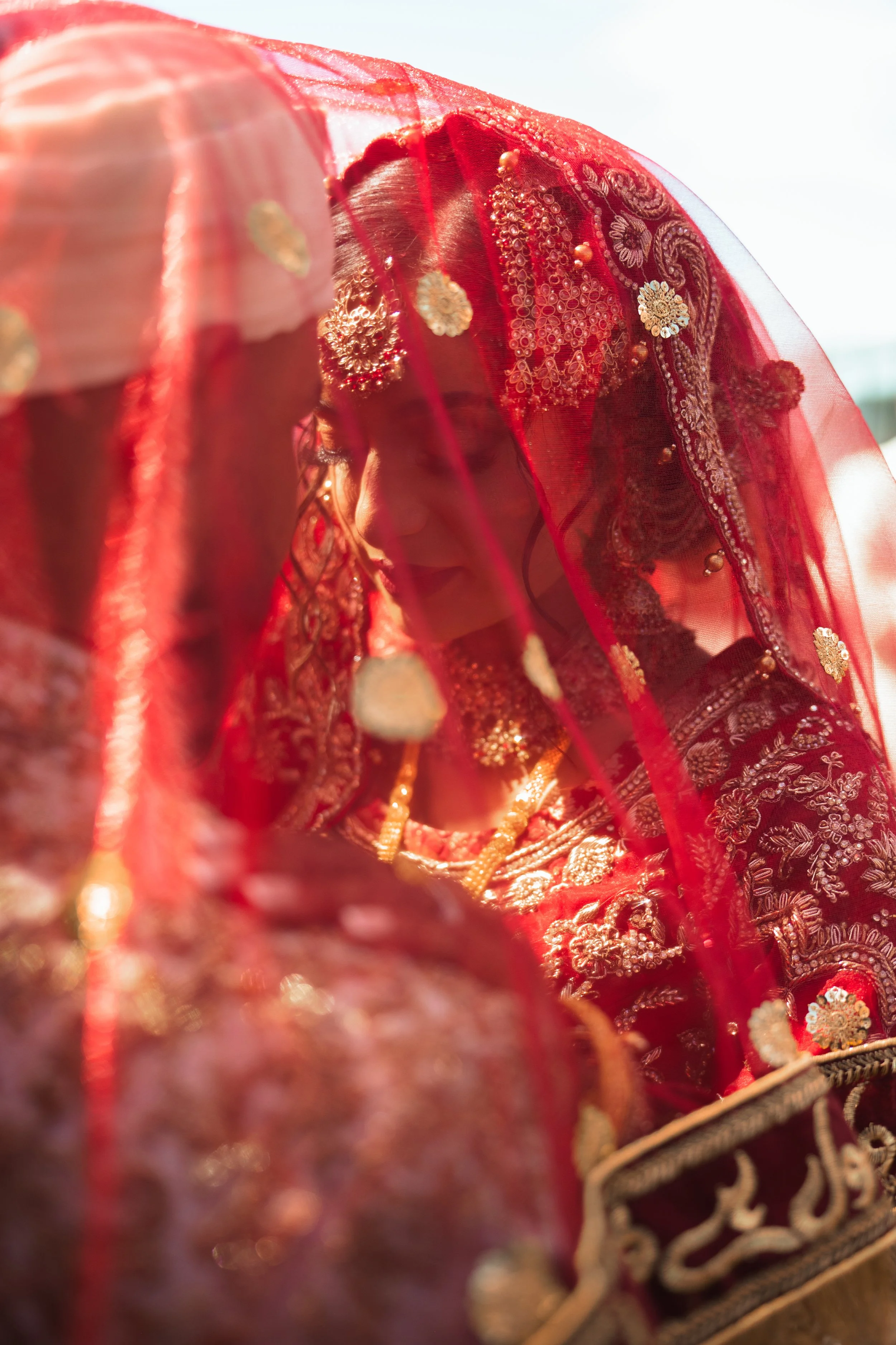 Bride and groom in traditional attire covered by red veil during wedding ceremony