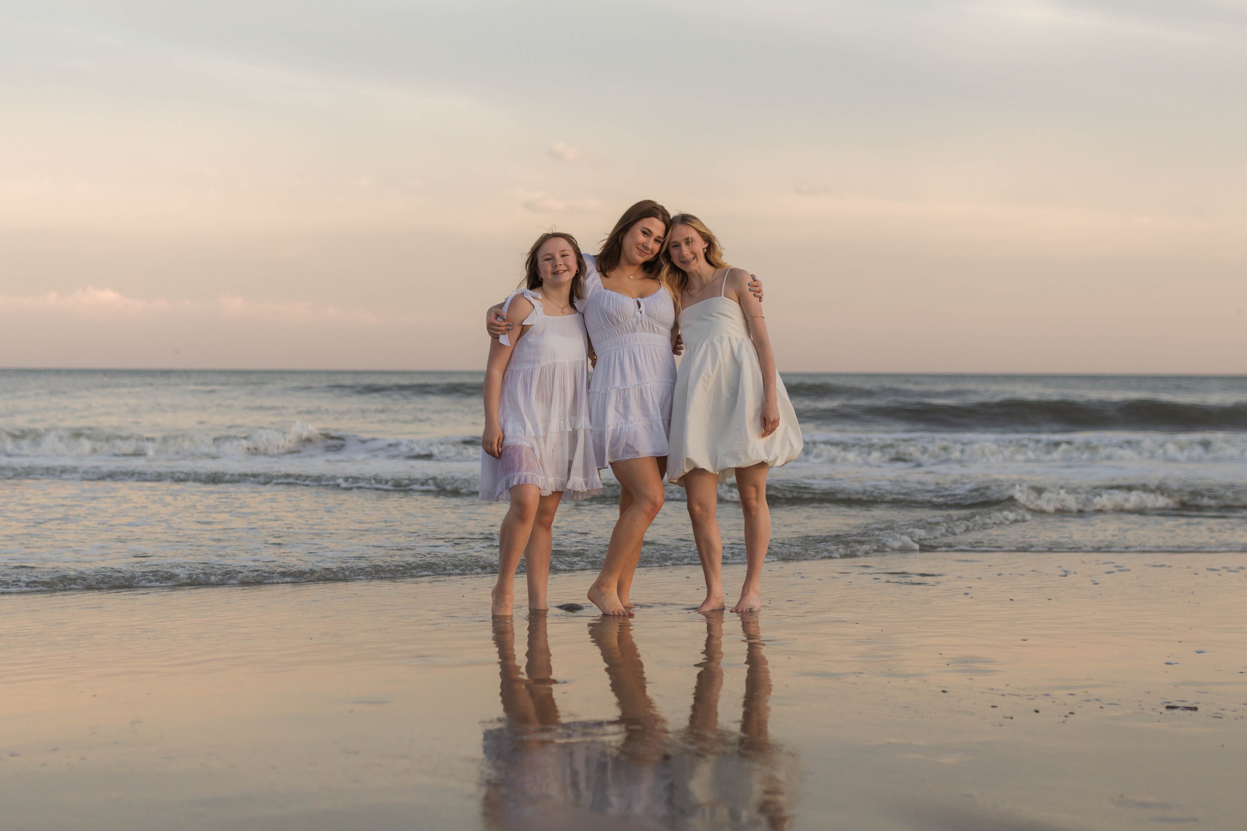 Mother and three daughters smiling and walking barefoot along the shoreline at sunset, Huntington Beach State Park