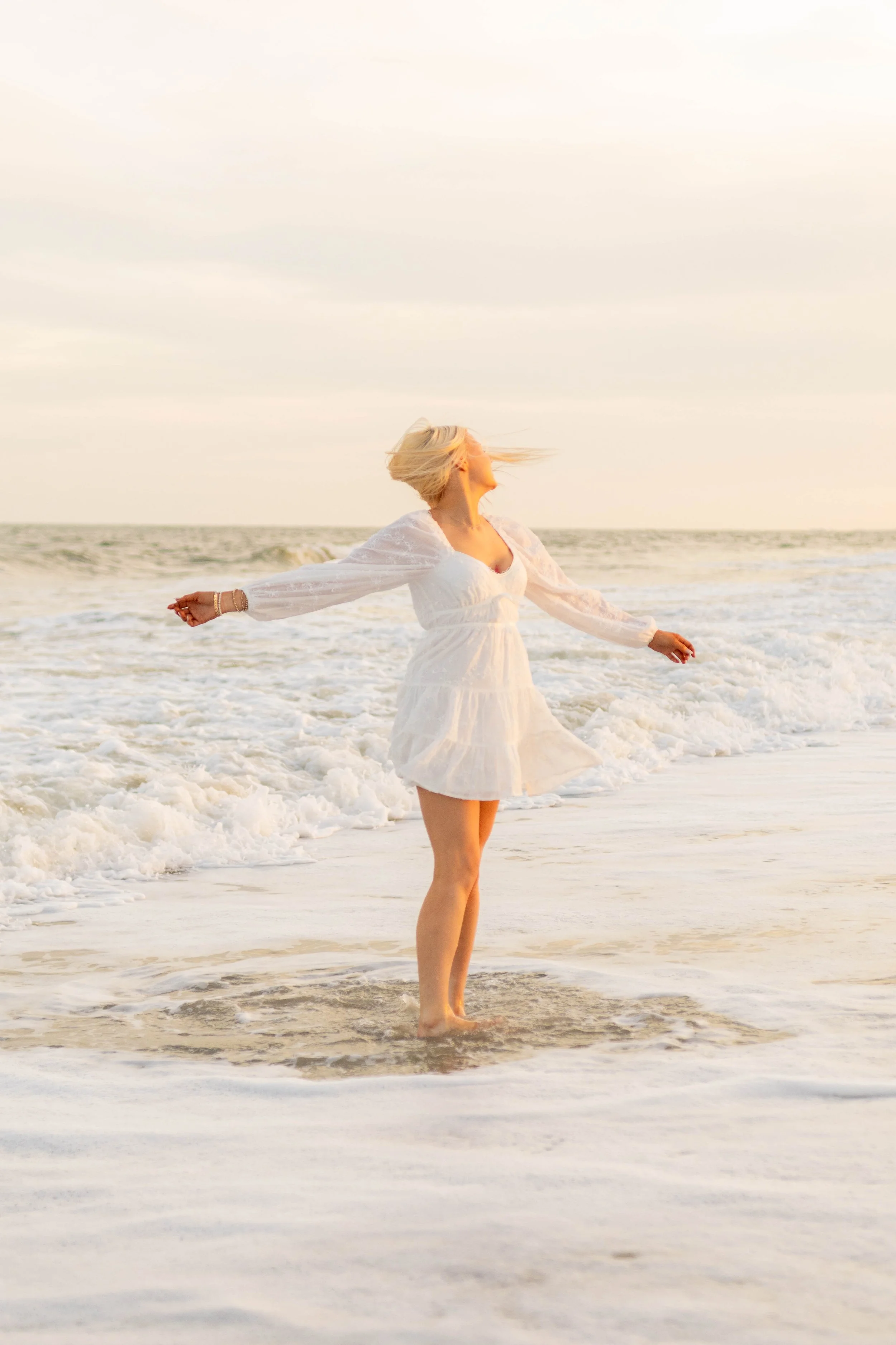 High school senior in Myrtle Beach wearing cap and gown during golden hour beach photo session, splashing in the water and smiling, taken by Myrtle Beach family and senior photographer.