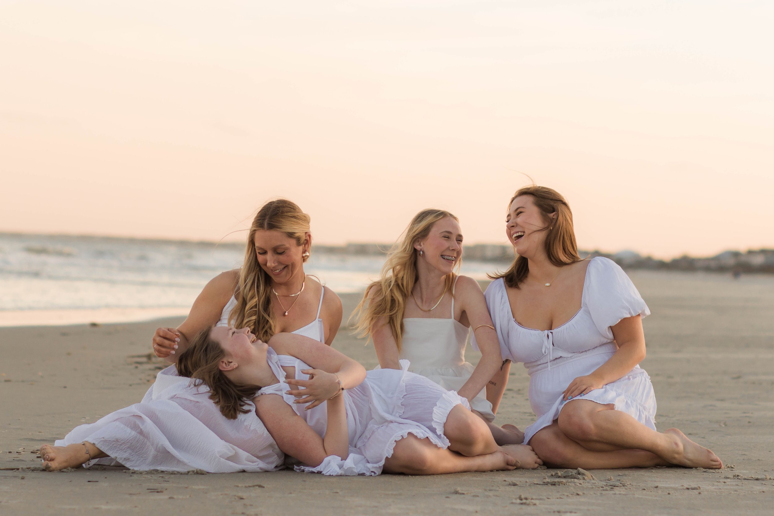 Mother and three daughters smiling and walking barefoot along the shoreline at sunset, Huntington Beach State Park