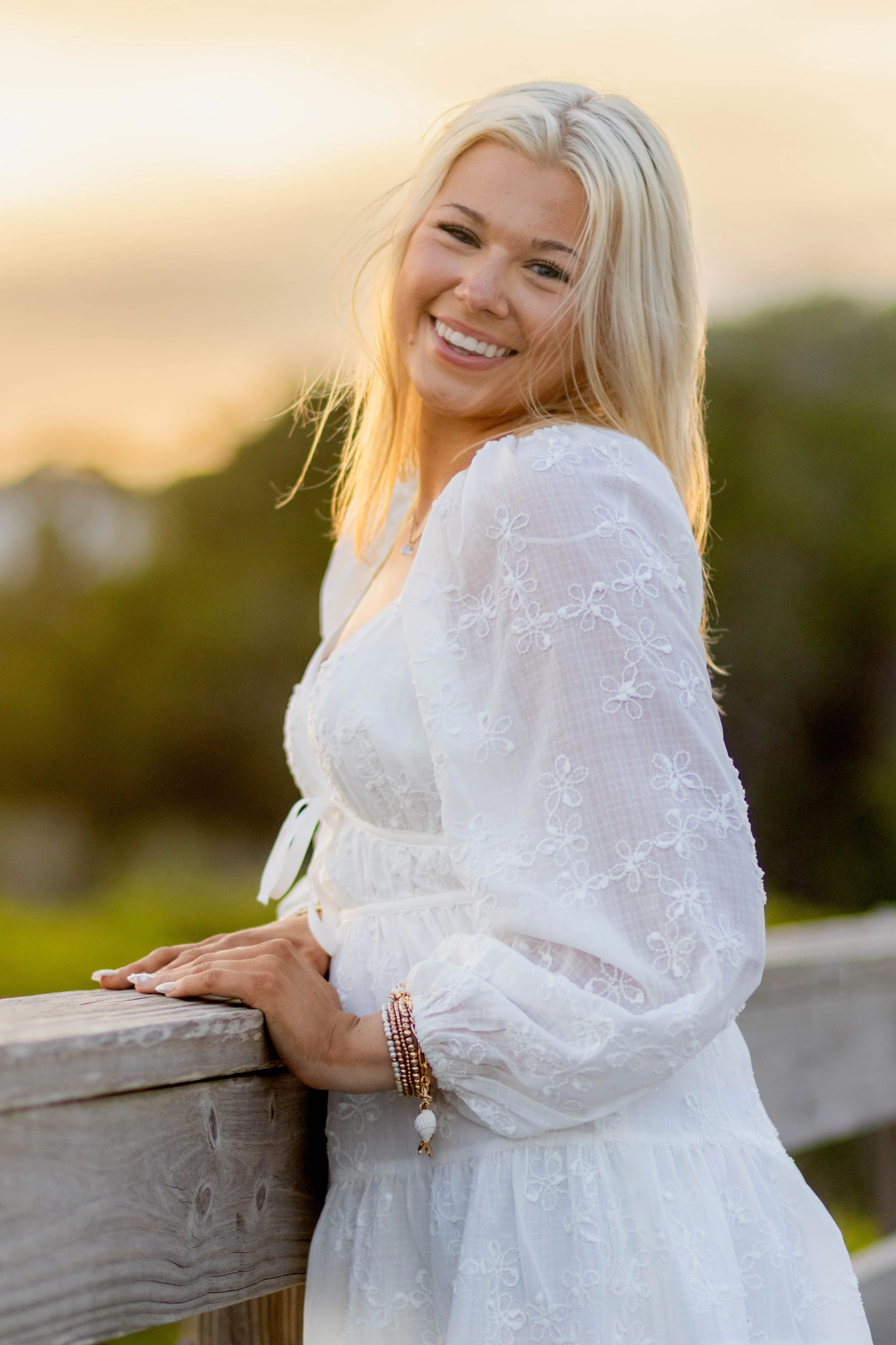 High school senior in Myrtle Beach wearing cap and gown during golden hour beach photo session, splashing in the water and smiling, taken by Myrtle Beach family and senior photographer.