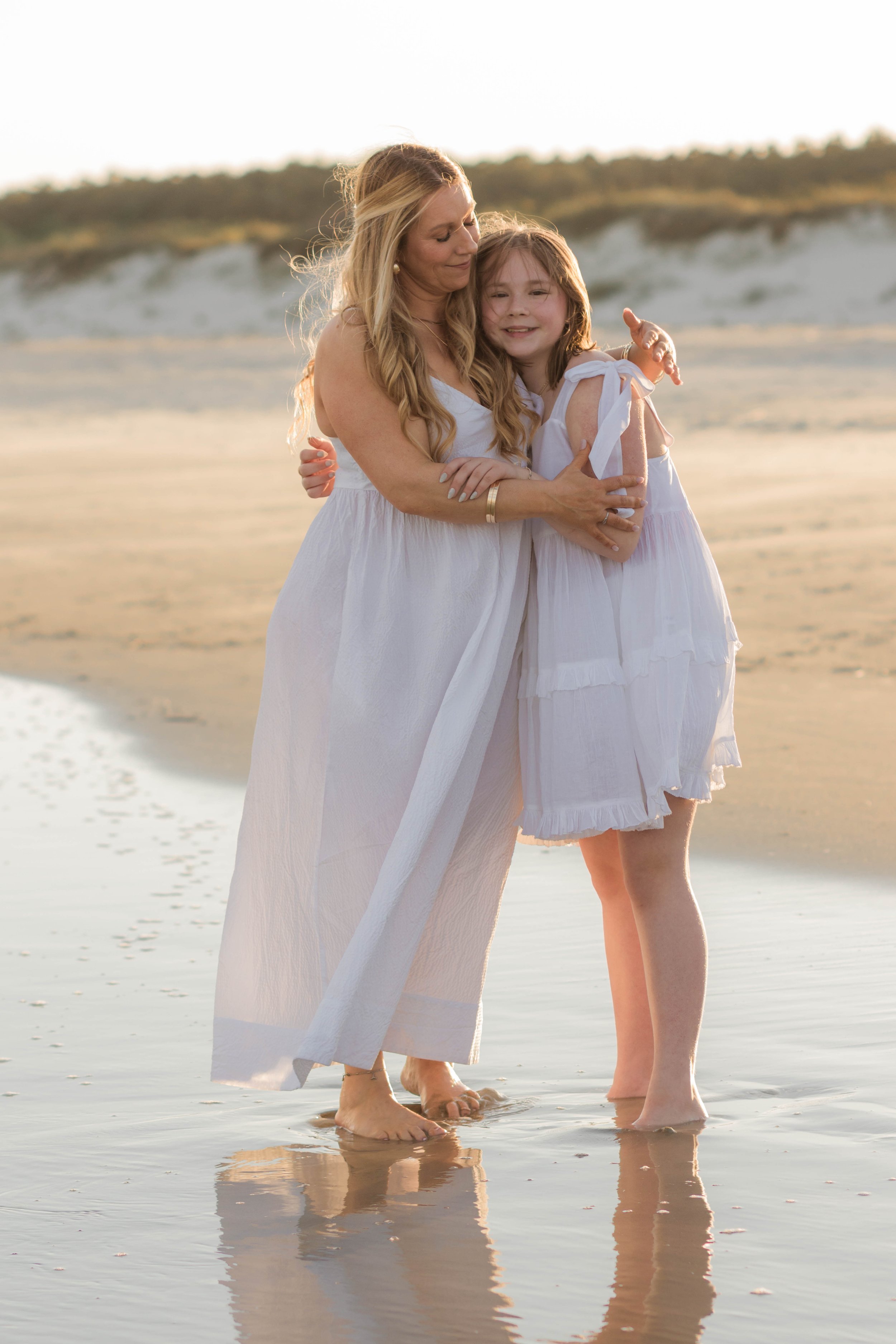Mother and three daughters smiling and walking barefoot along the shoreline at sunset, Huntington Beach State Park