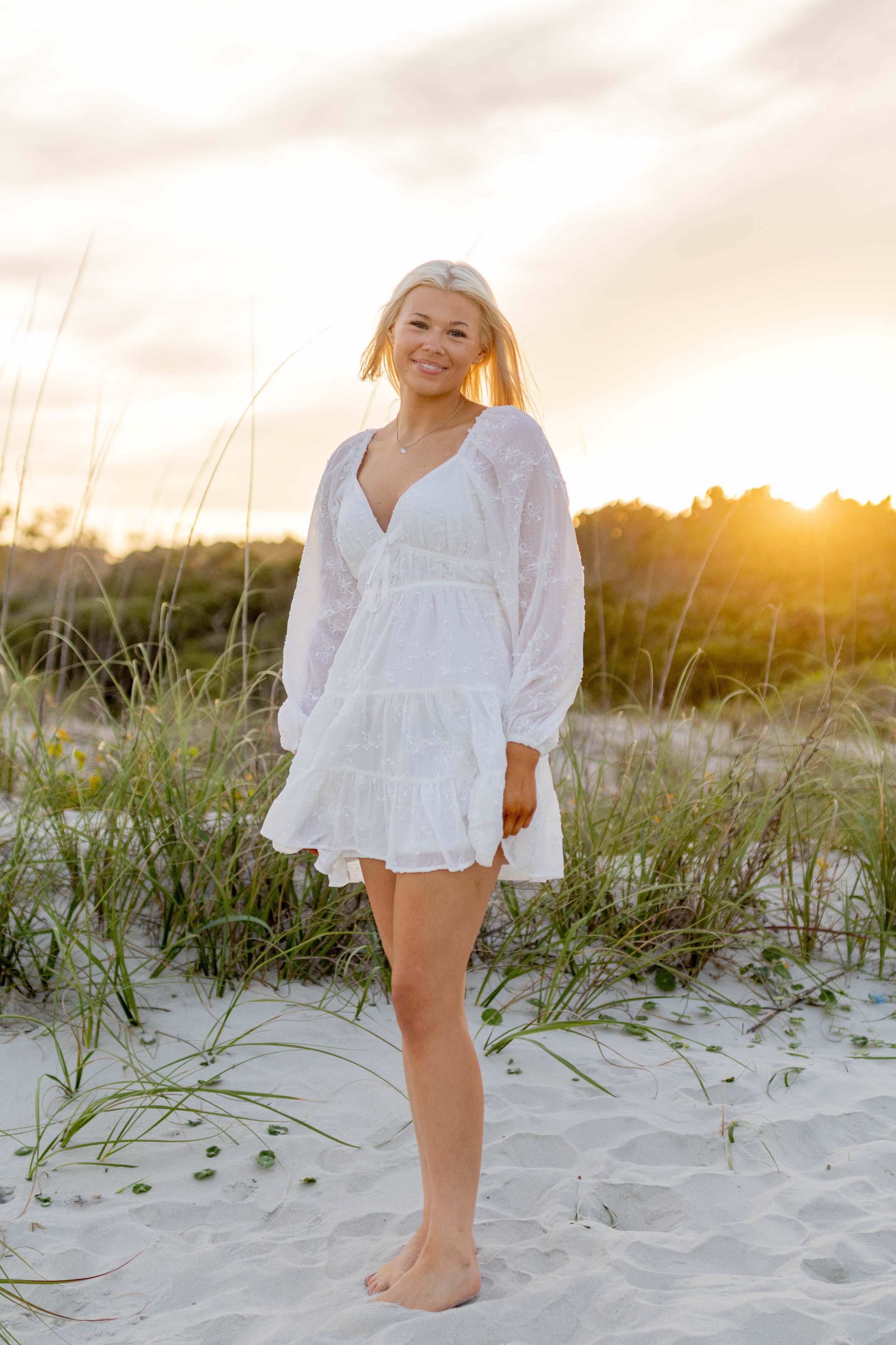 High school senior in Myrtle Beach wearing cap and gown during golden hour beach photo session, splashing in the water and smiling, taken by Myrtle Beach family and senior photographer.