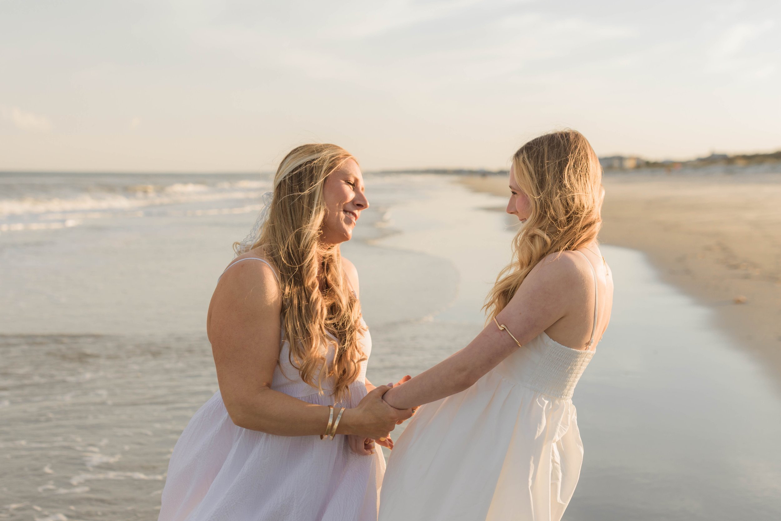 Mother and three daughters smiling and walking barefoot along the shoreline at sunset, Huntington Beach State Park