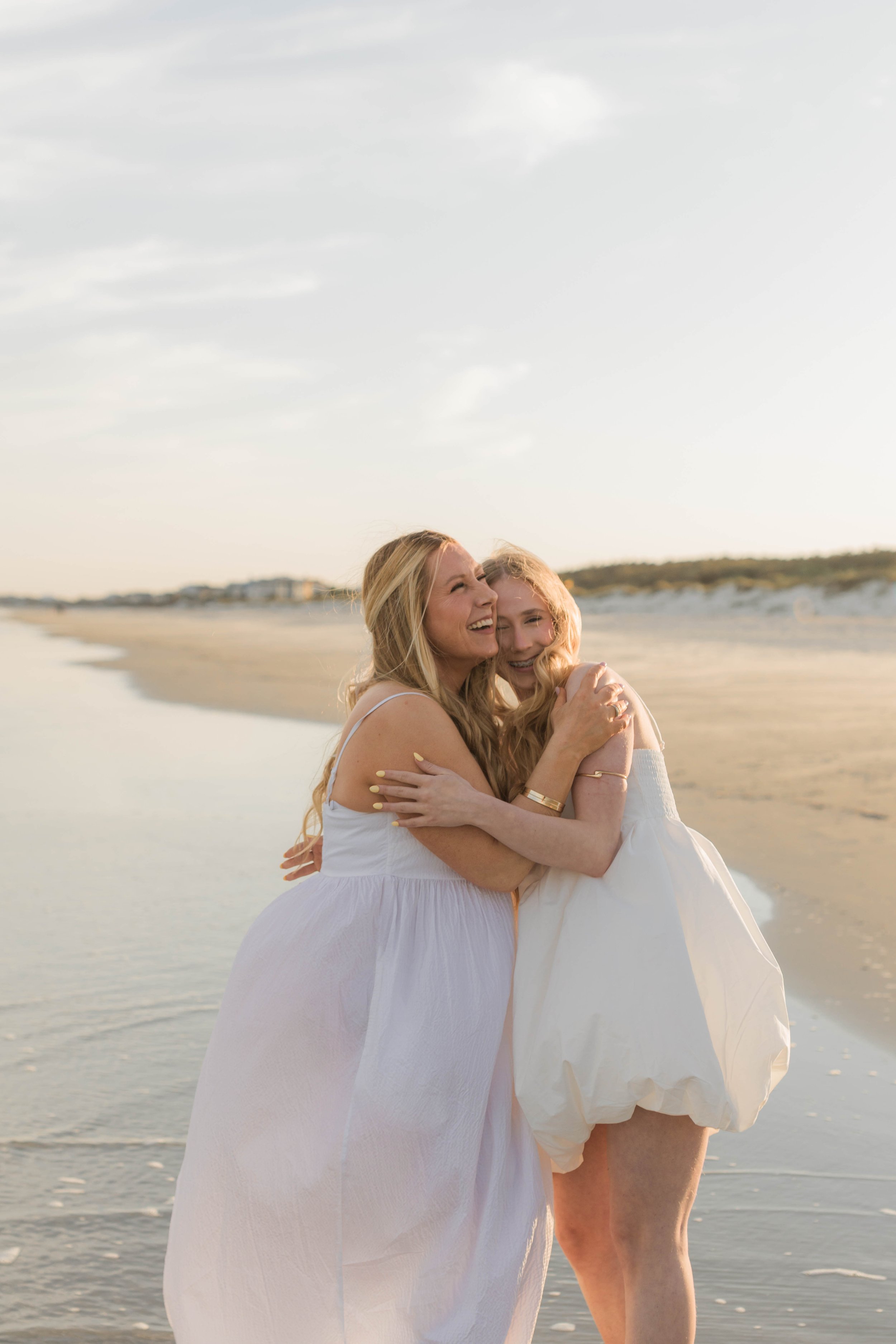 Mother and three daughters smiling and walking barefoot along the shoreline at sunset, Huntington Beach State Park