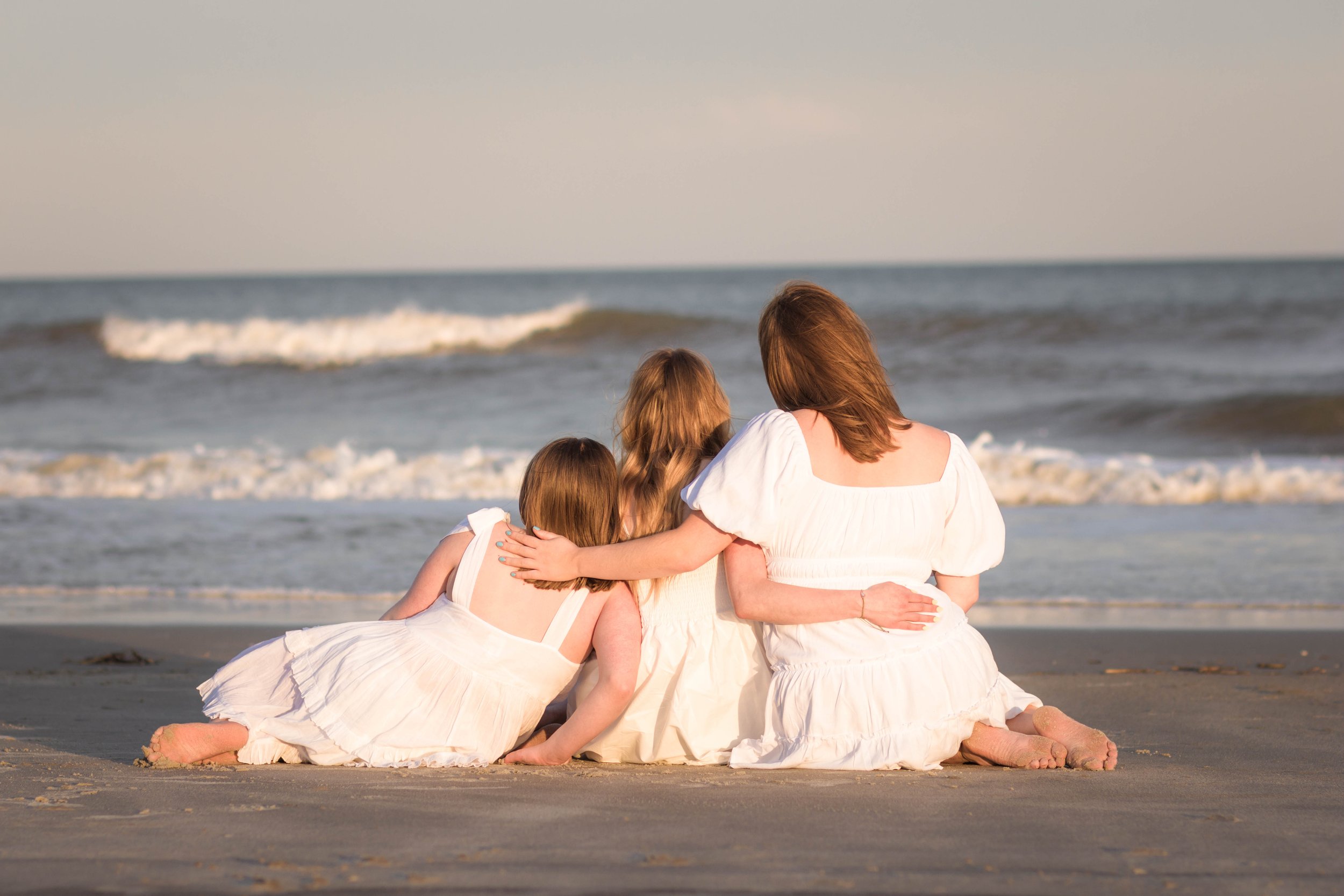 Mother and three daughters smiling and walking barefoot along the shoreline at sunset, Huntington Beach State Park