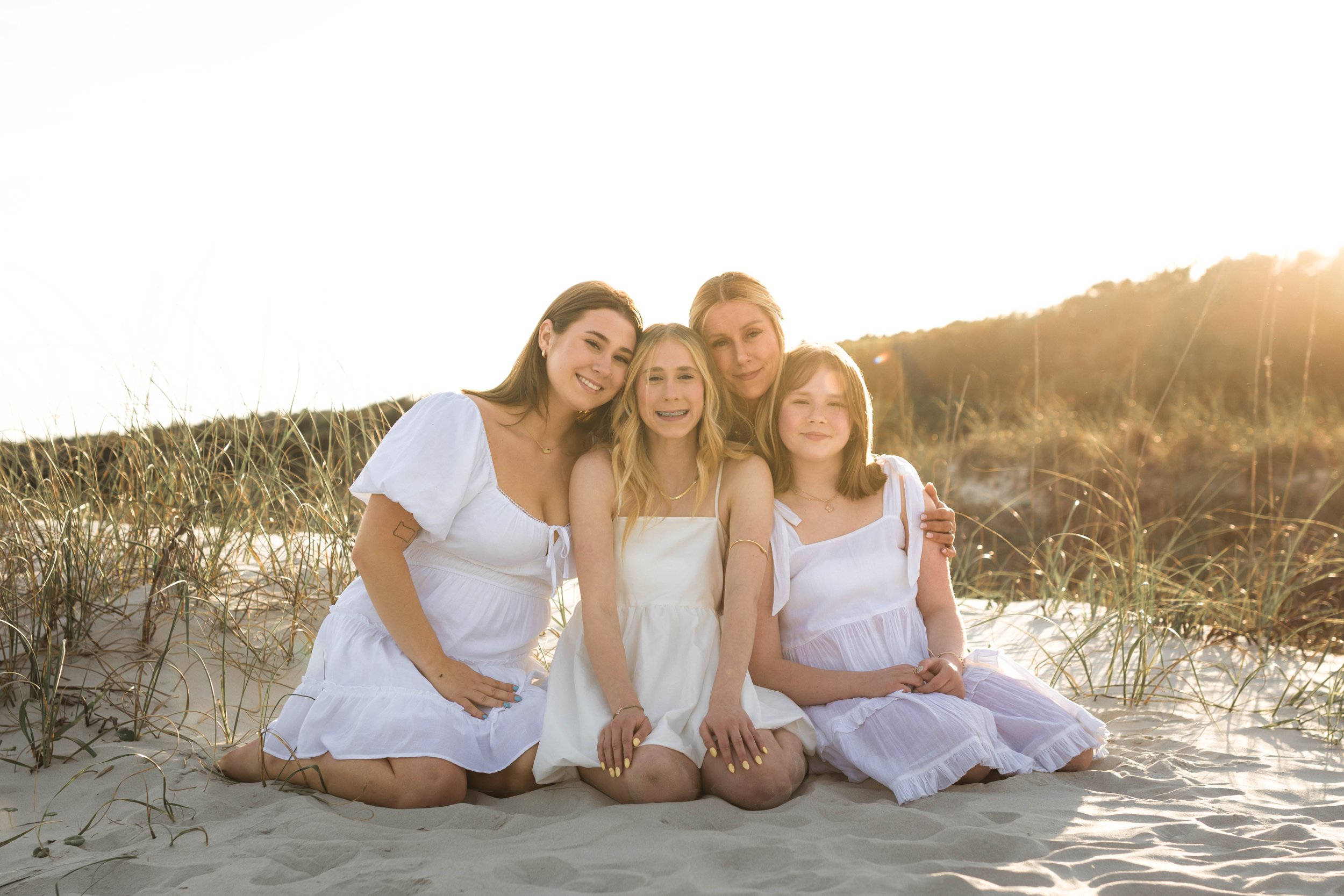 Mother and three daughters smiling and walking barefoot along the shoreline at sunset, Huntington Beach State Park