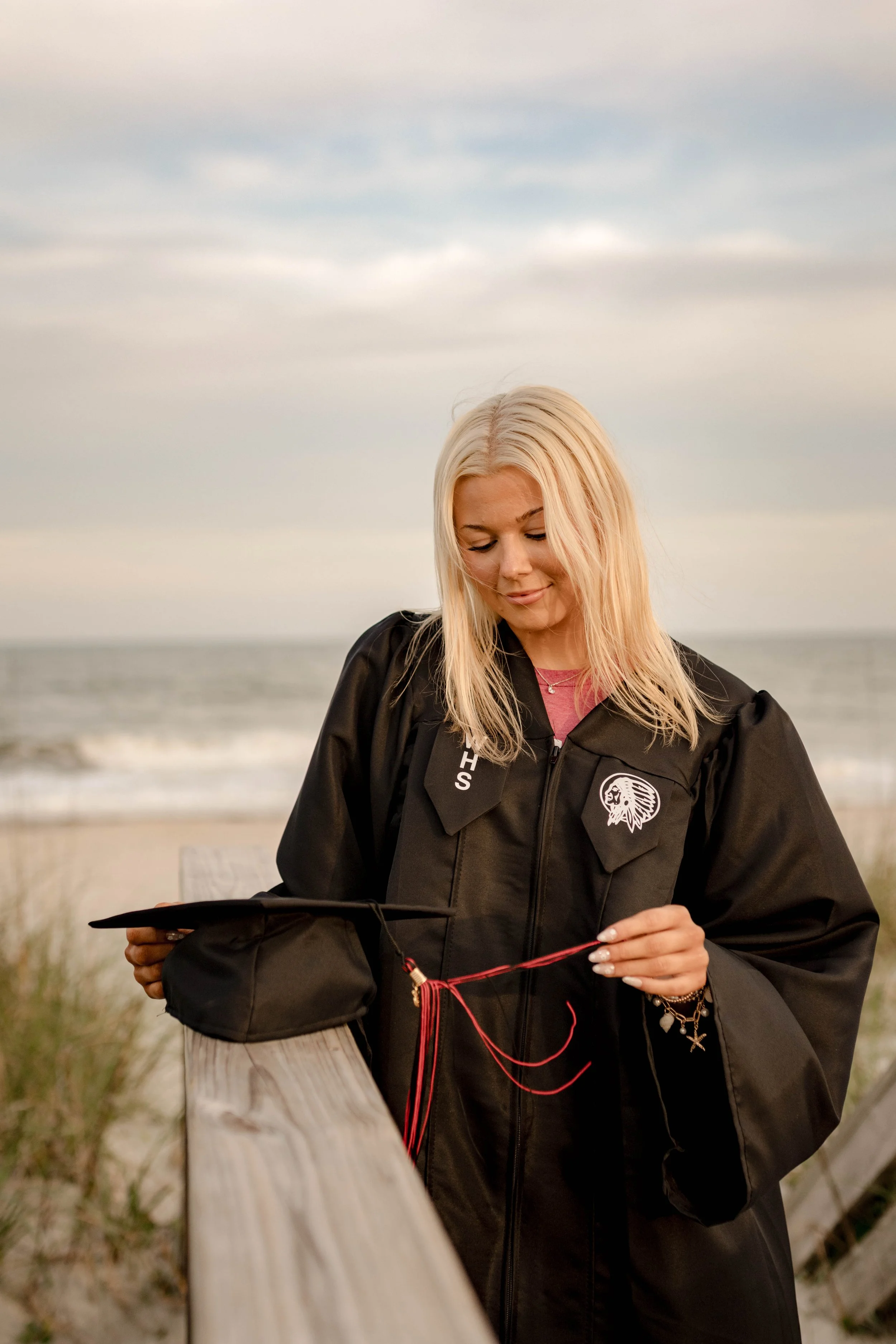 High school senior in Myrtle Beach wearing cap and gown during golden hour beach photo session, splashing in the water and smiling, taken by Myrtle Beach family and senior photographer.