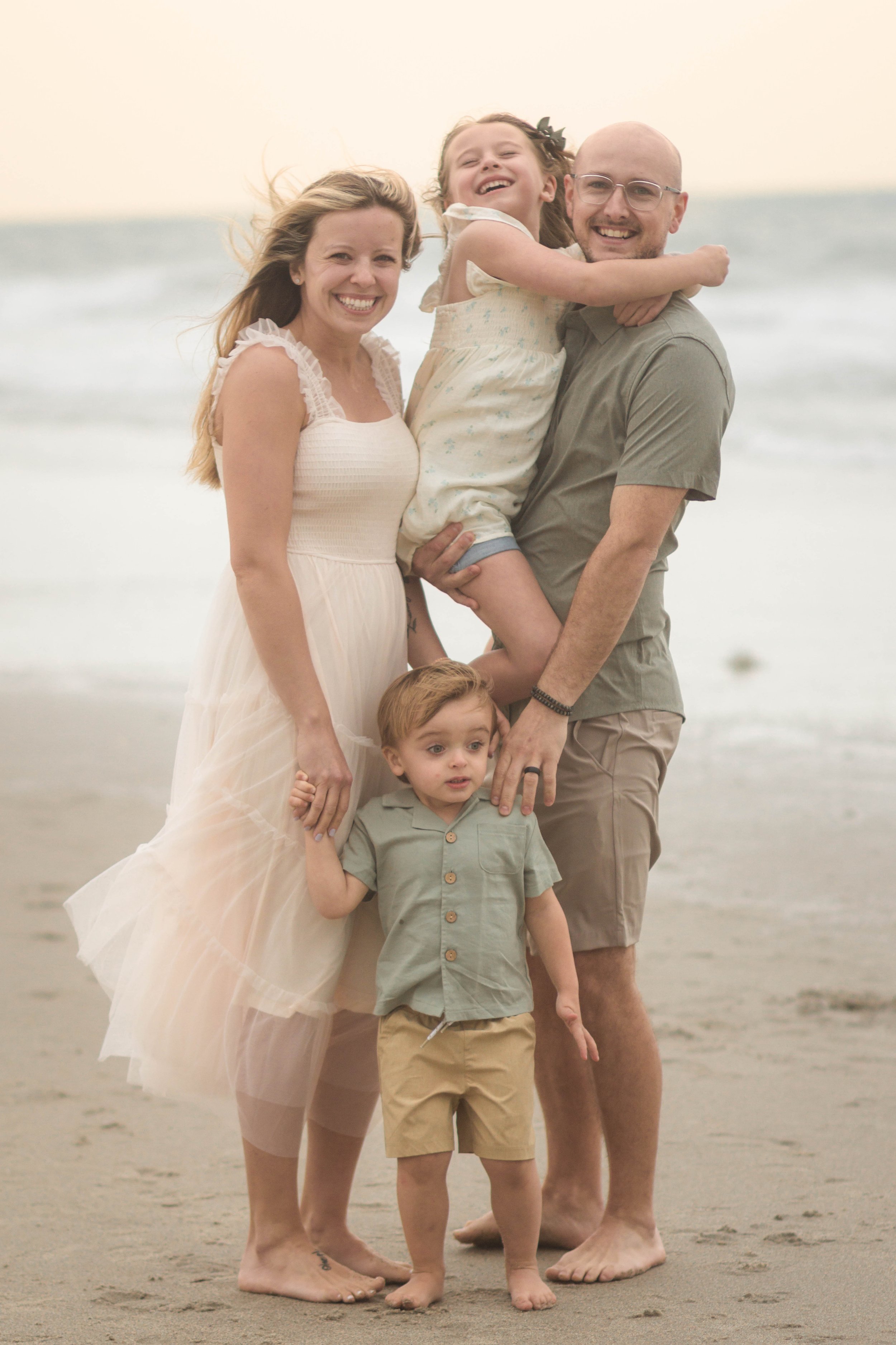 Family cuddling together during a windy beach photo session at Springmaid Pier in Myrtle Beach.