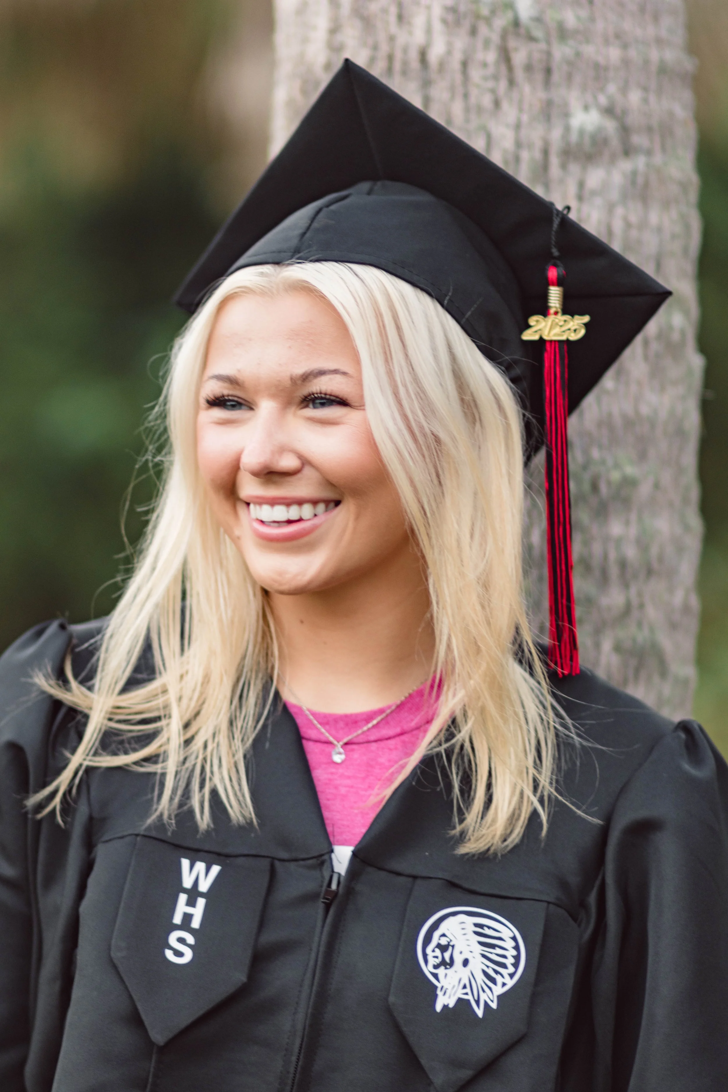 High school senior in Myrtle Beach wearing cap and gown during golden hour beach photo session, splashing in the water and smiling, taken by Myrtle Beach family and senior photographer.