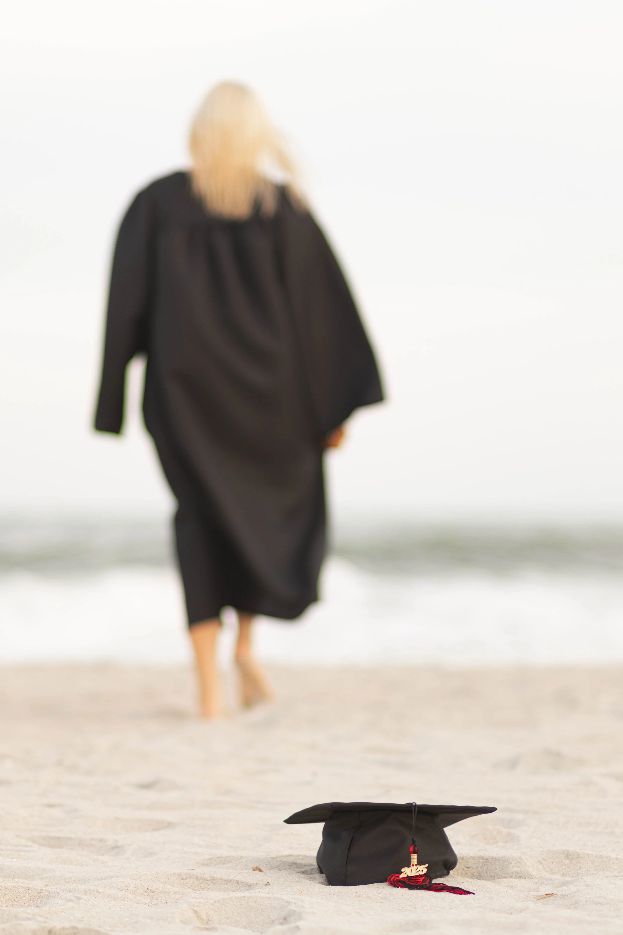 High school senior in Myrtle Beach wearing cap and gown during golden hour beach photo session, splashing in the water and smiling, taken by Myrtle Beach family and senior photographer.