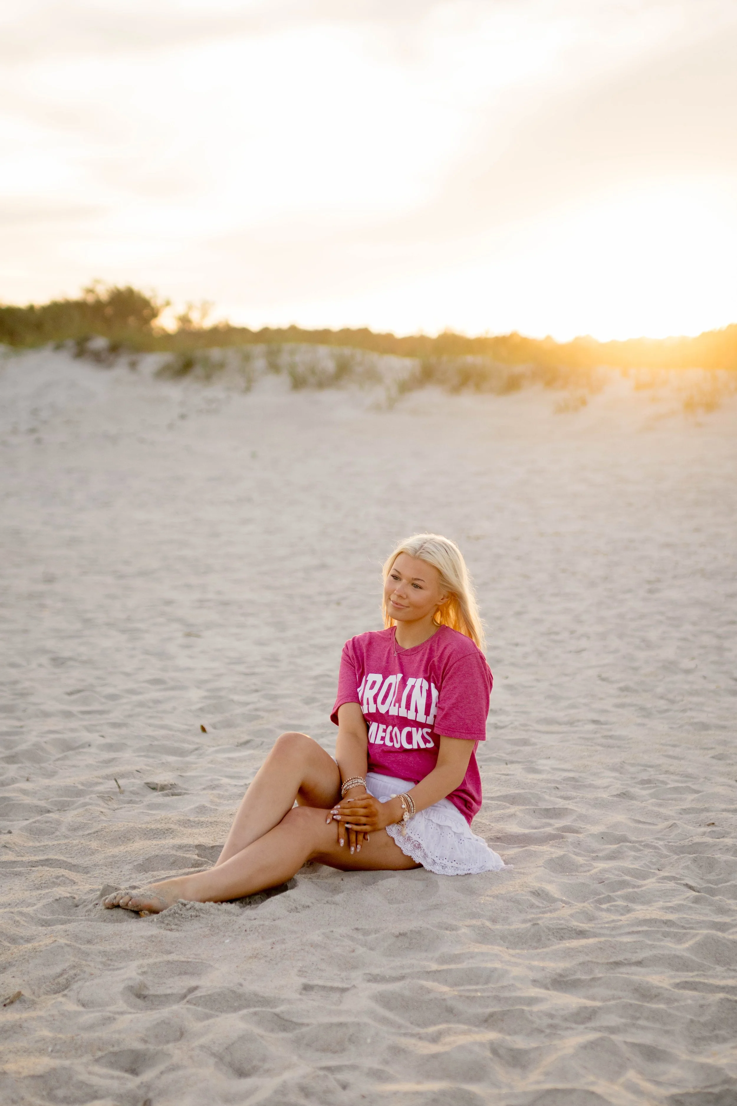 High school senior in Myrtle Beach wearing cap and gown during golden hour beach photo session, splashing in the water and smiling, taken by Myrtle Beach family and senior photographer.