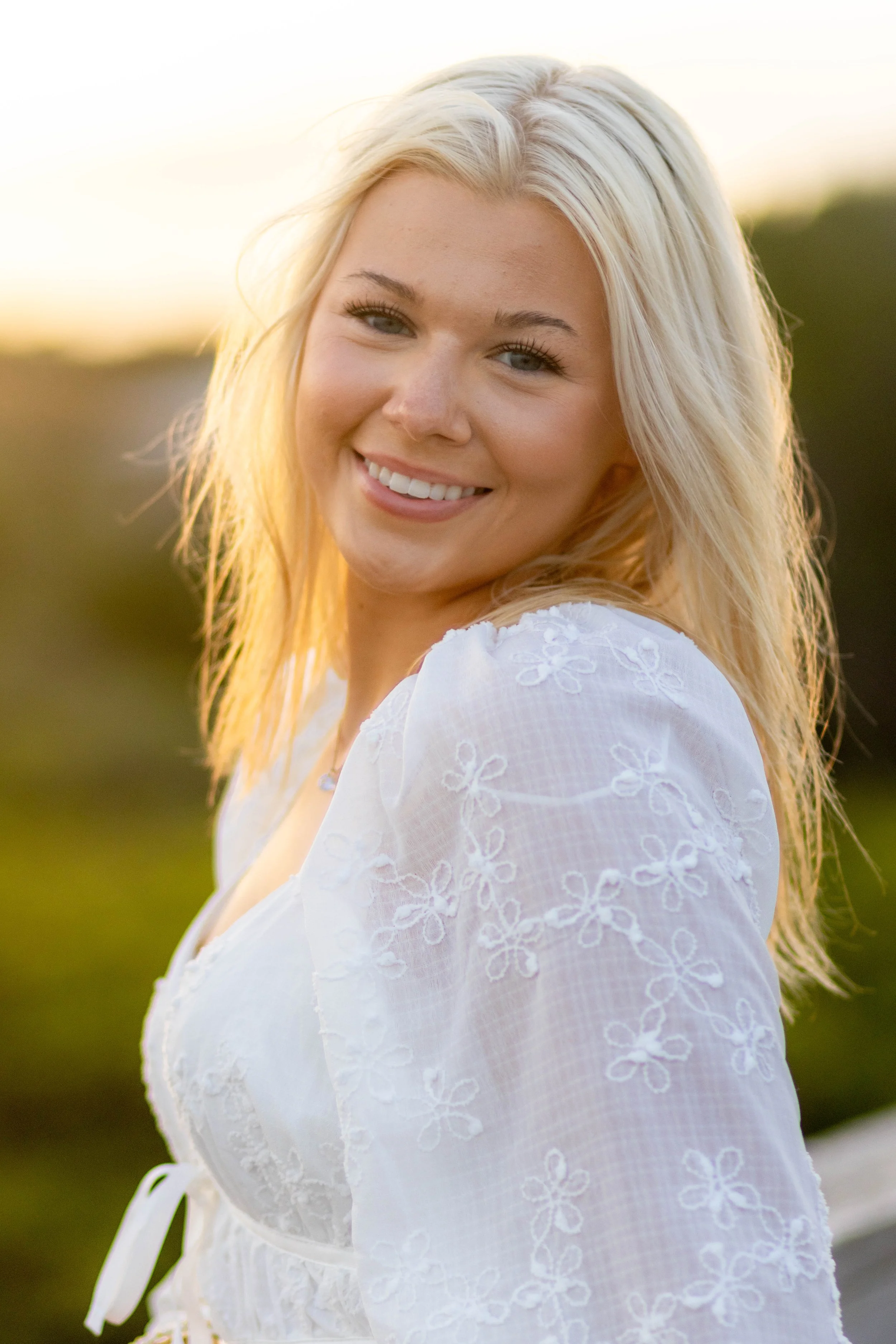 High school senior in Myrtle Beach wearing cap and gown during golden hour beach photo session, splashing in the water and smiling, taken by Myrtle Beach family and senior photographer.