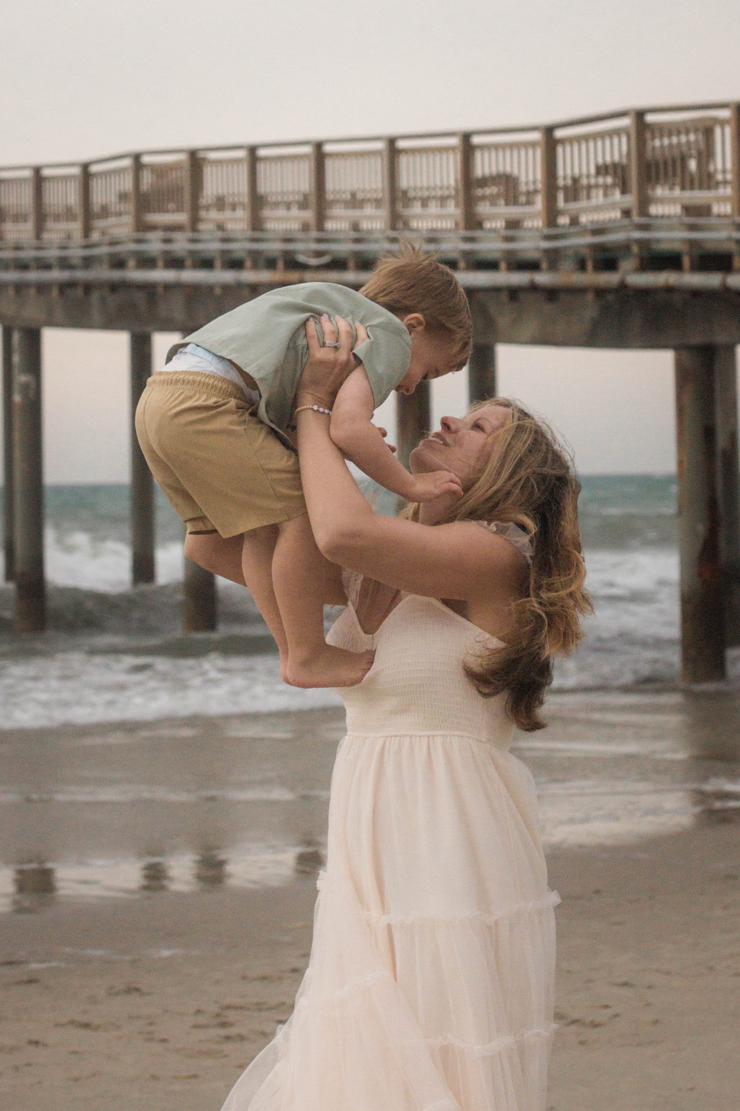 Family playing together during a windy beach photo session at Springmaid Pier in Myrtle Beach.