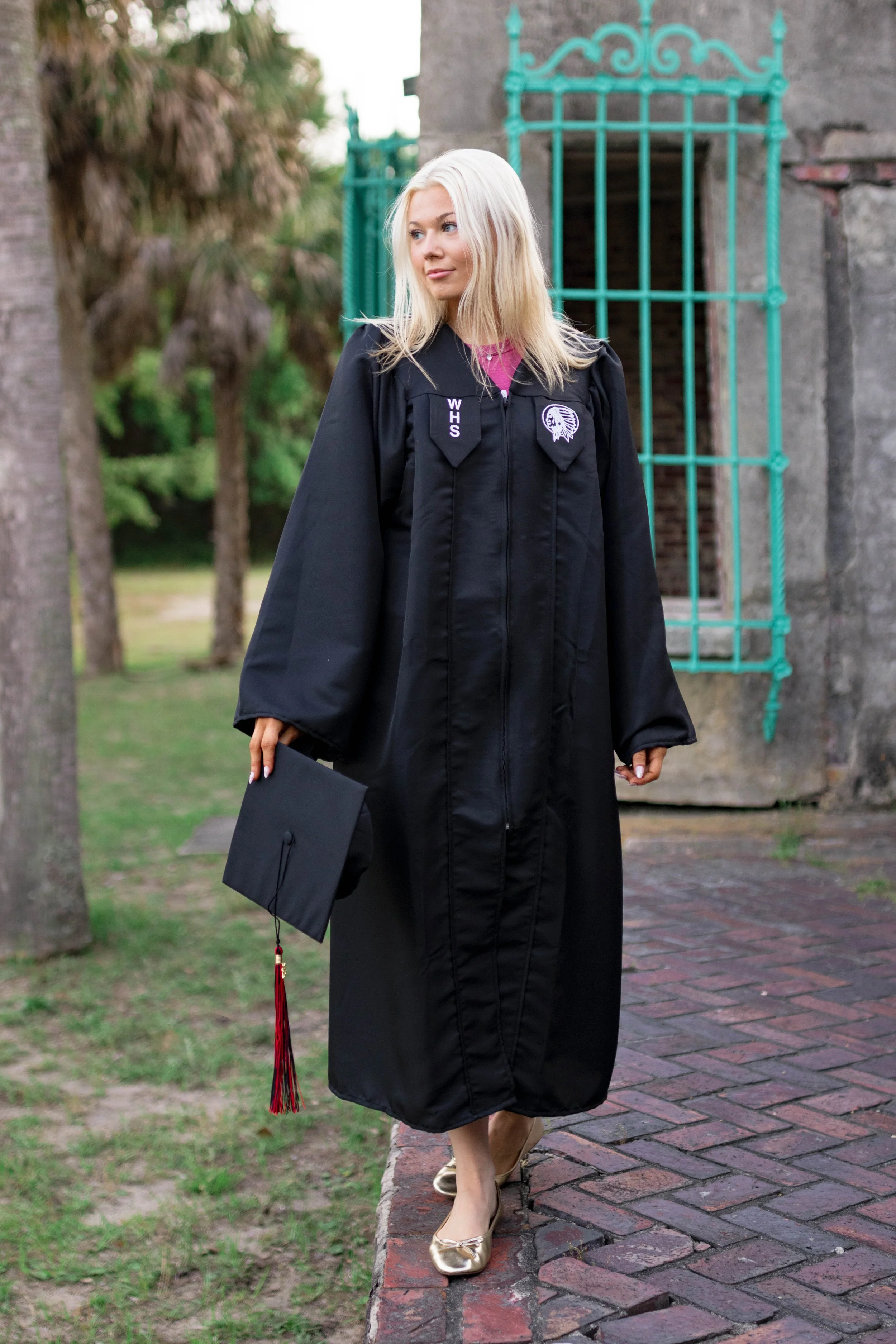 High school senior in Myrtle Beach wearing cap and gown during golden hour beach photo session, splashing in the water and smiling, taken by Myrtle Beach family and senior photographer.