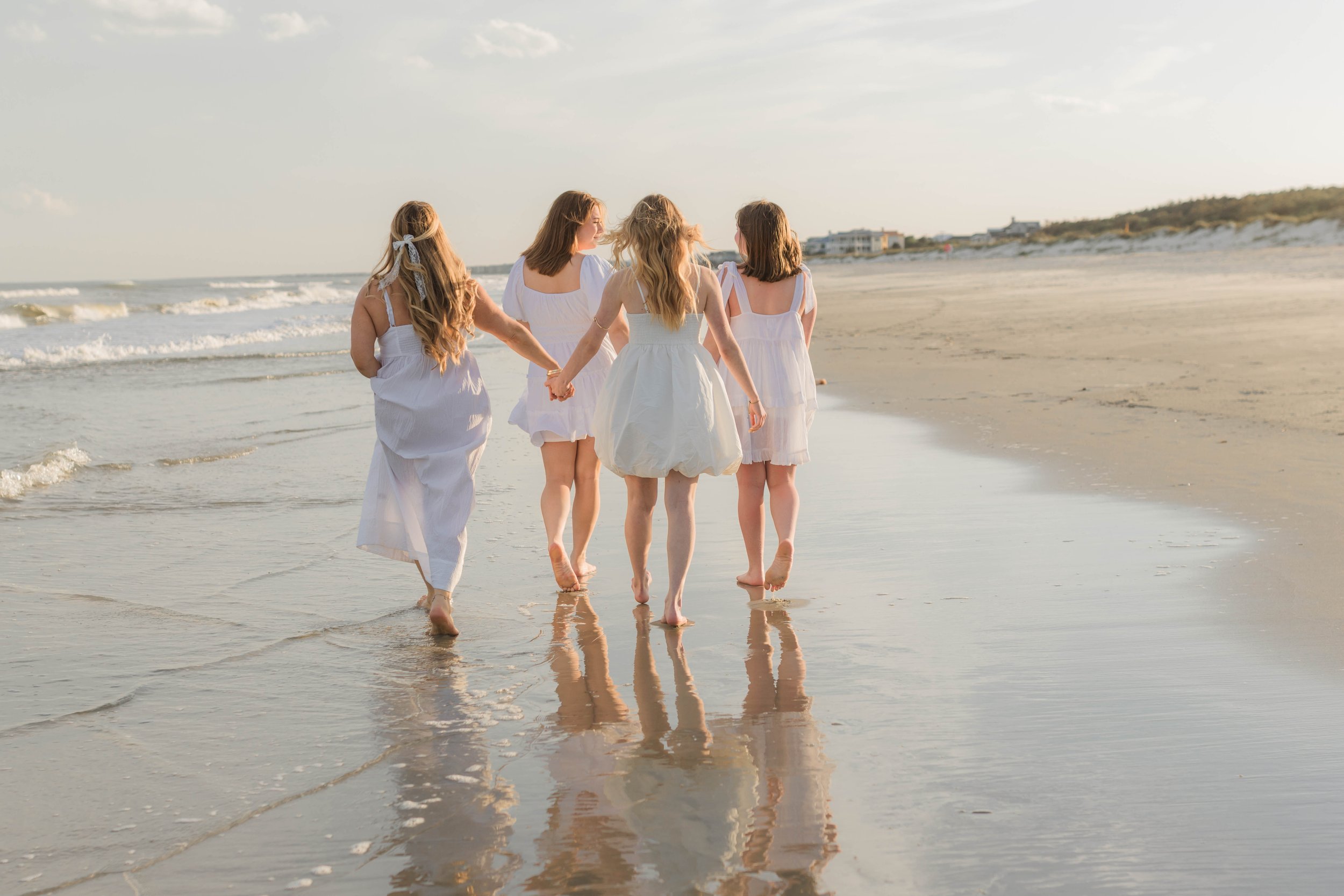 Mother and three daughters smiling and walking barefoot along the shoreline at sunset, Huntington Beach State Park
