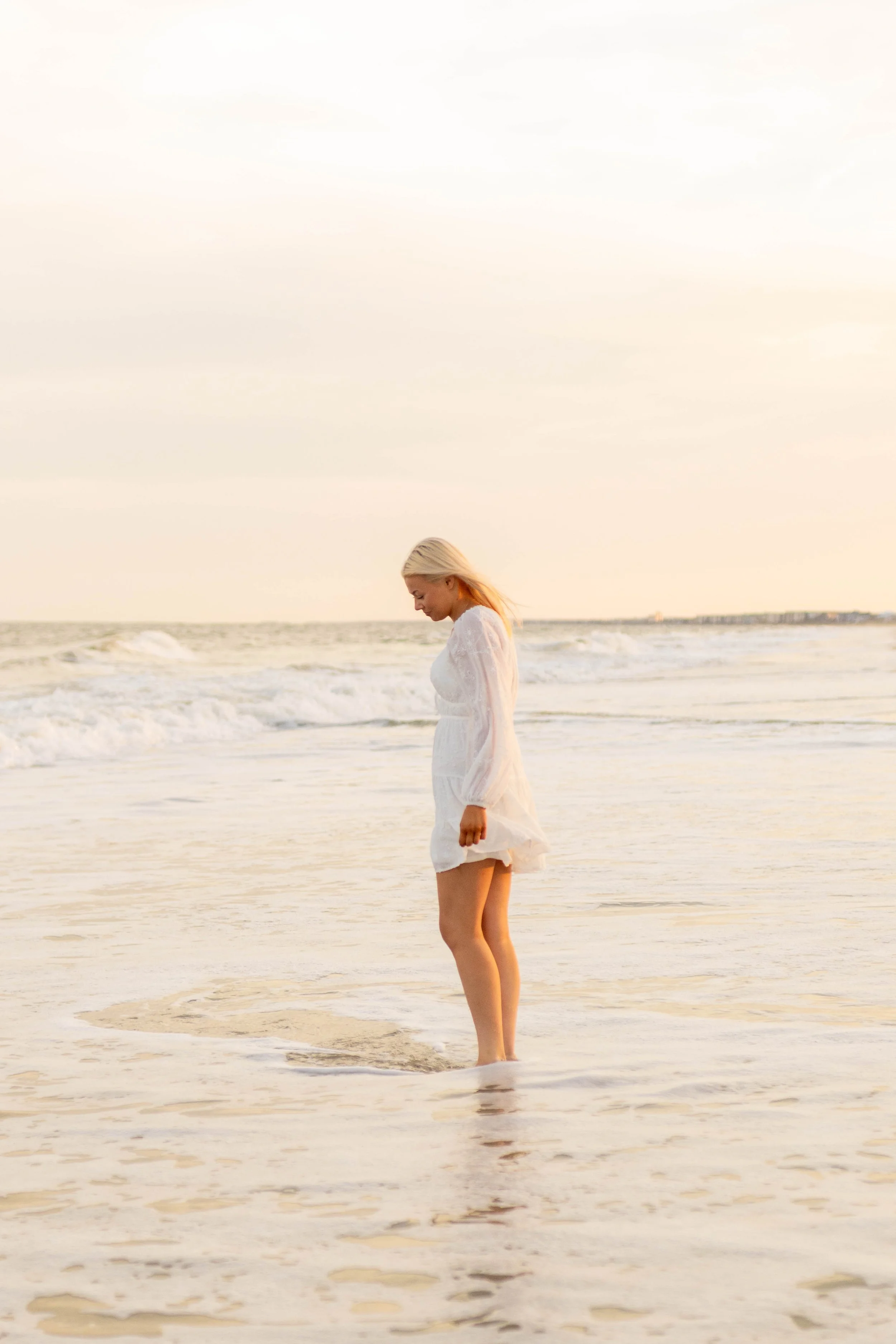 High school senior in Myrtle Beach wearing cap and gown during golden hour beach photo session, splashing in the water and smiling, taken by Myrtle Beach family and senior photographer.
