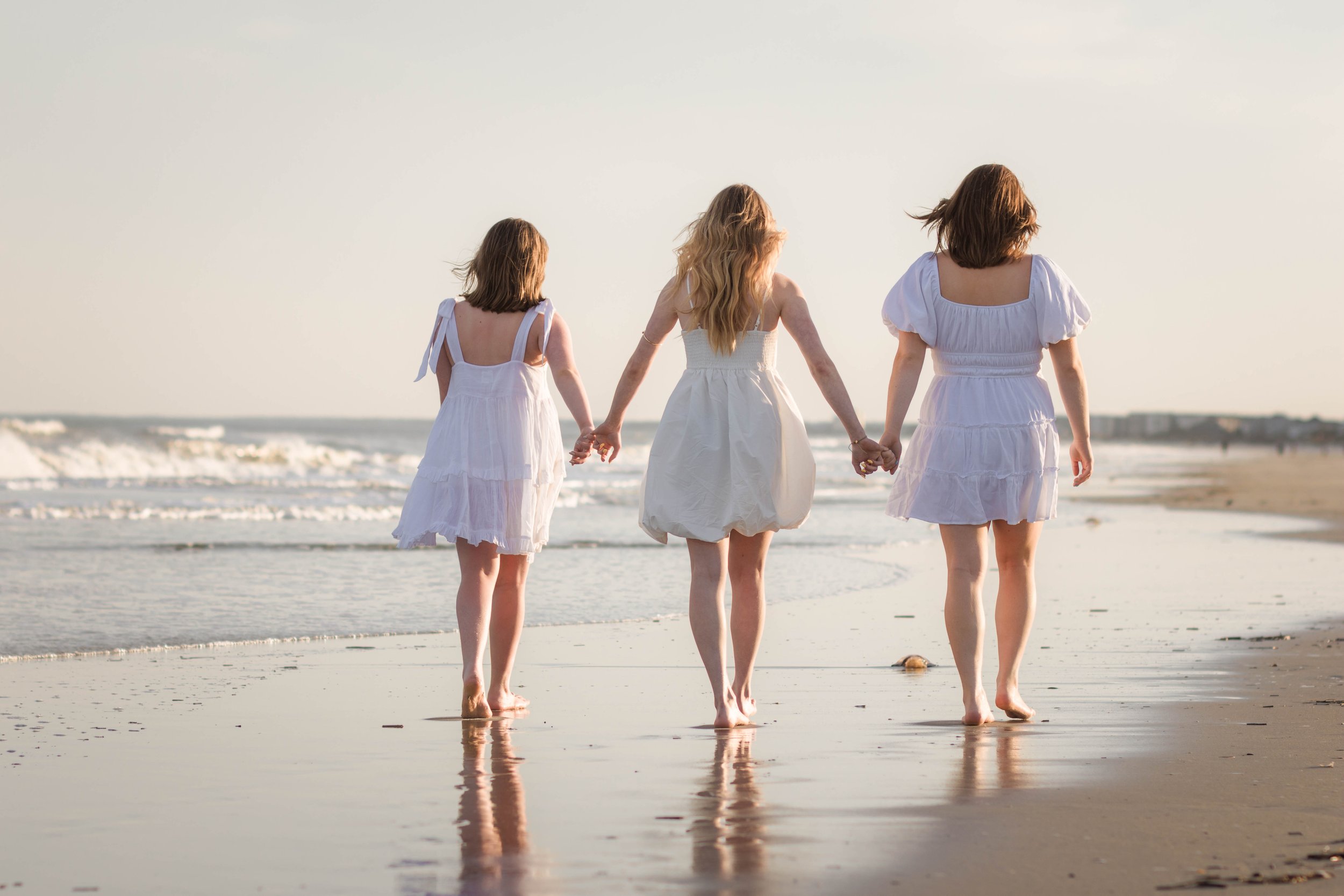 Mother and three daughters smiling and walking barefoot along the shoreline at sunset, Huntington Beach State Park