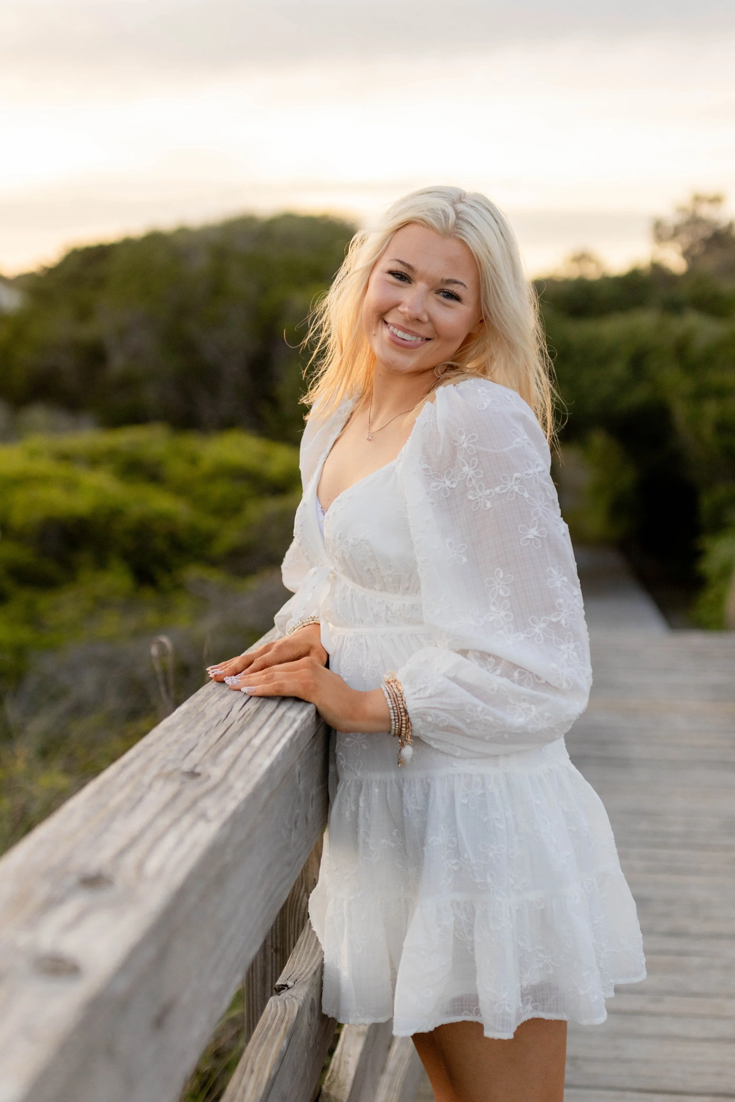 High school senior in Myrtle Beach wearing cap and gown during golden hour beach photo session, splashing in the water and smiling, taken by Myrtle Beach family and senior photographer.