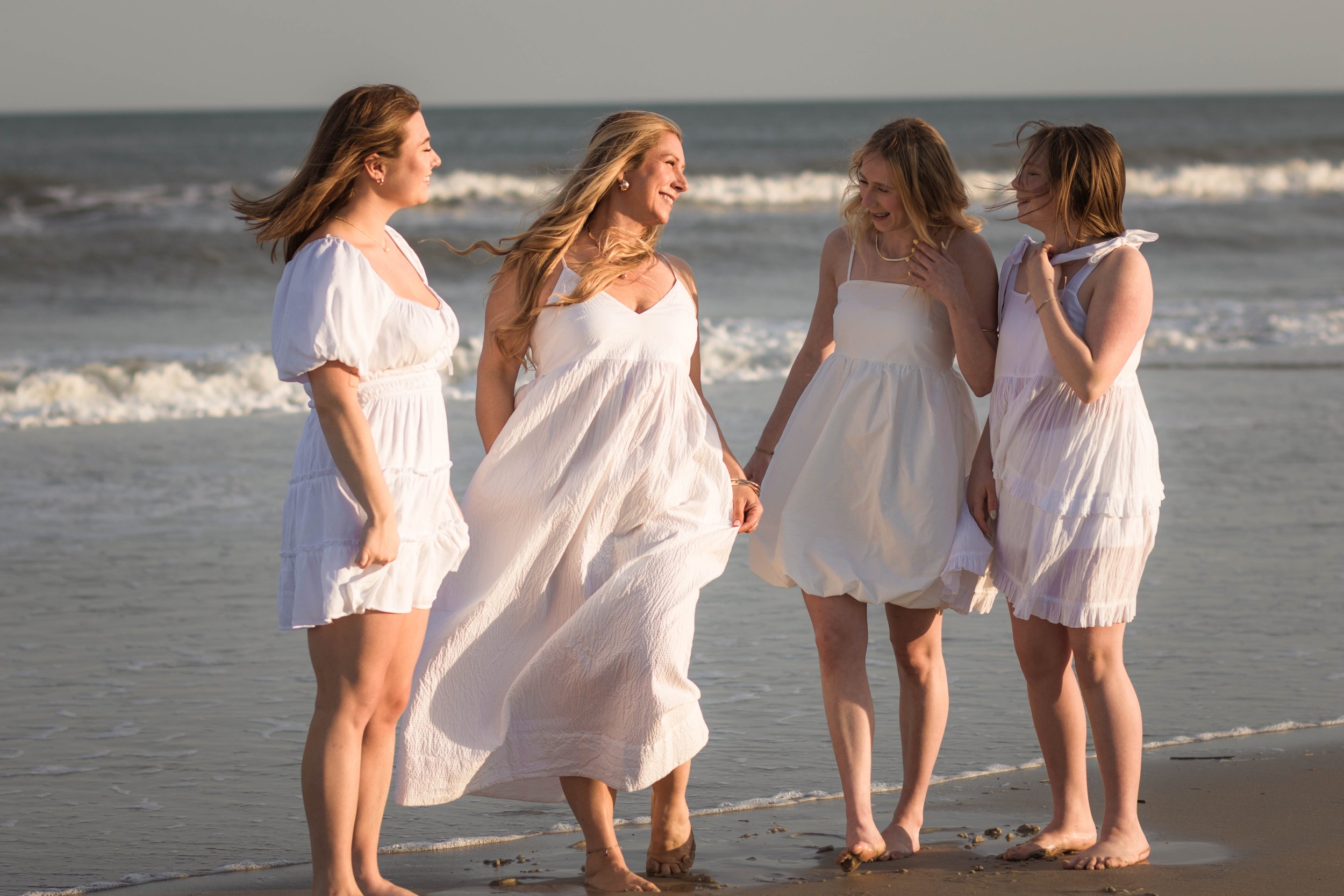 Mother and three daughters smiling and walking barefoot along the shoreline at sunset, Huntington Beach State Park