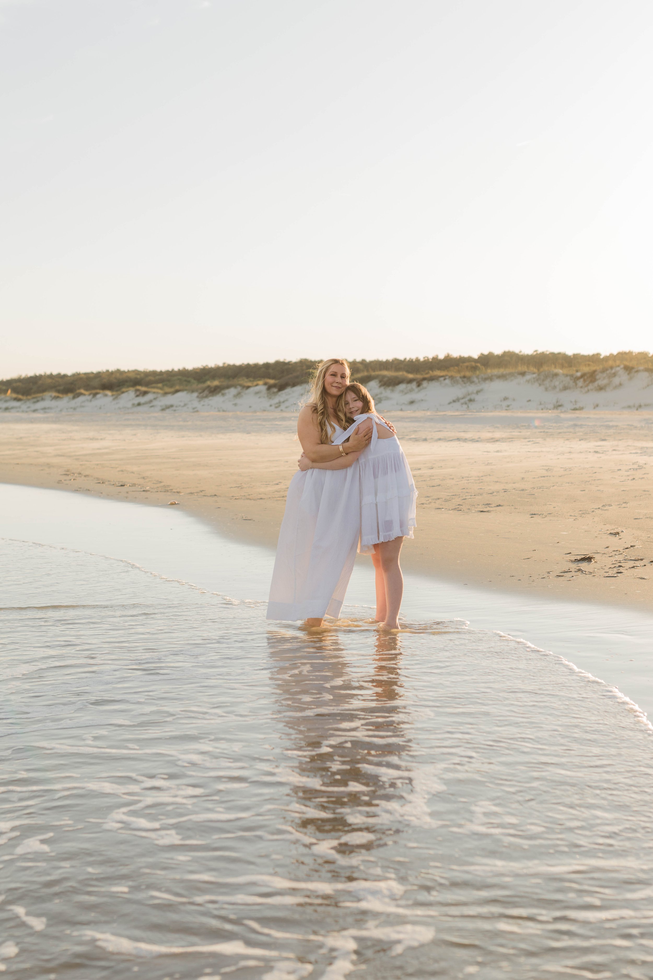 Mother and three daughters smiling and walking barefoot along the shoreline at sunset, Huntington Beach State Park