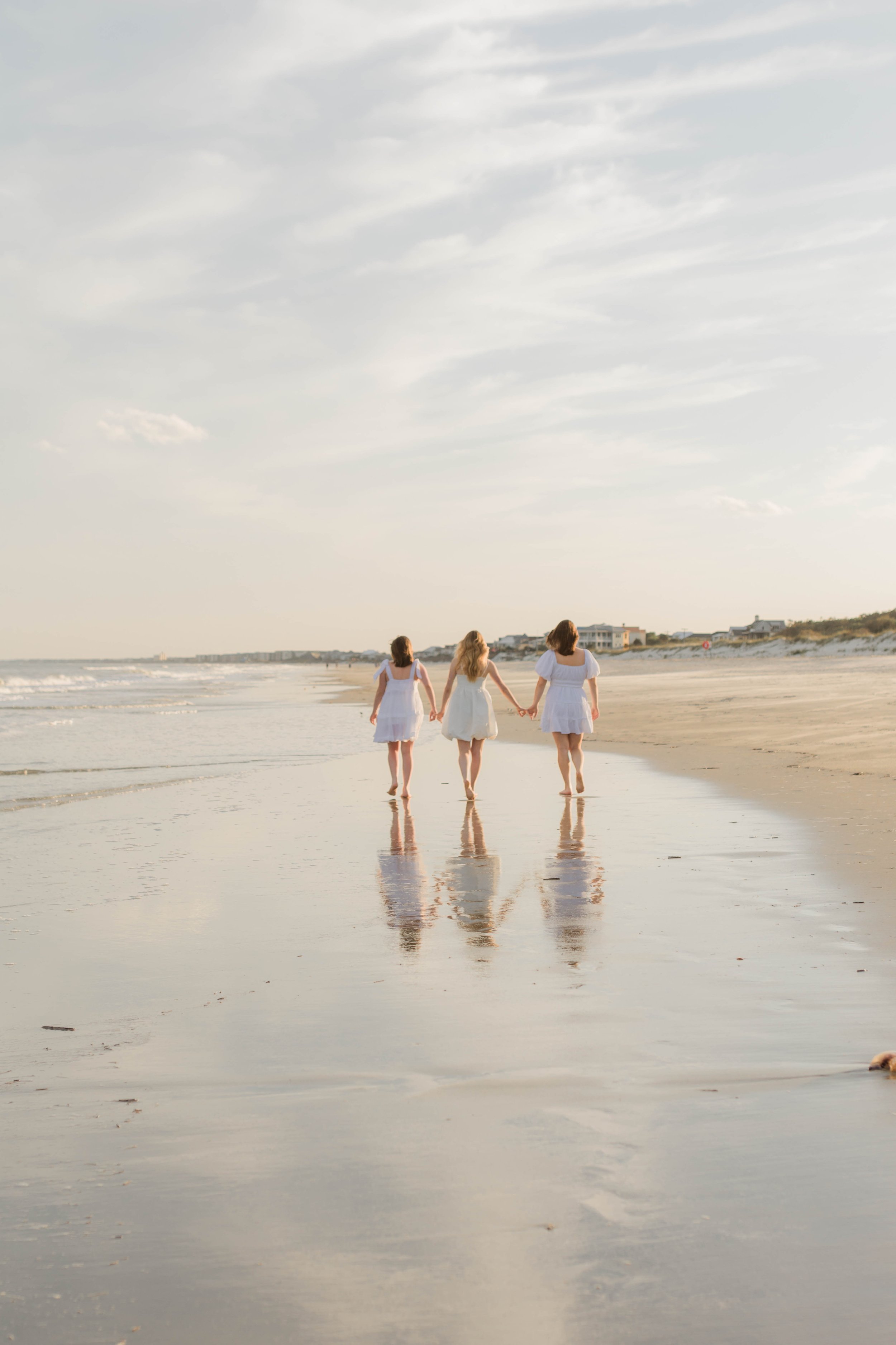 Mother and three daughters smiling and walking barefoot along the shoreline at sunset, Huntington Beach State Park