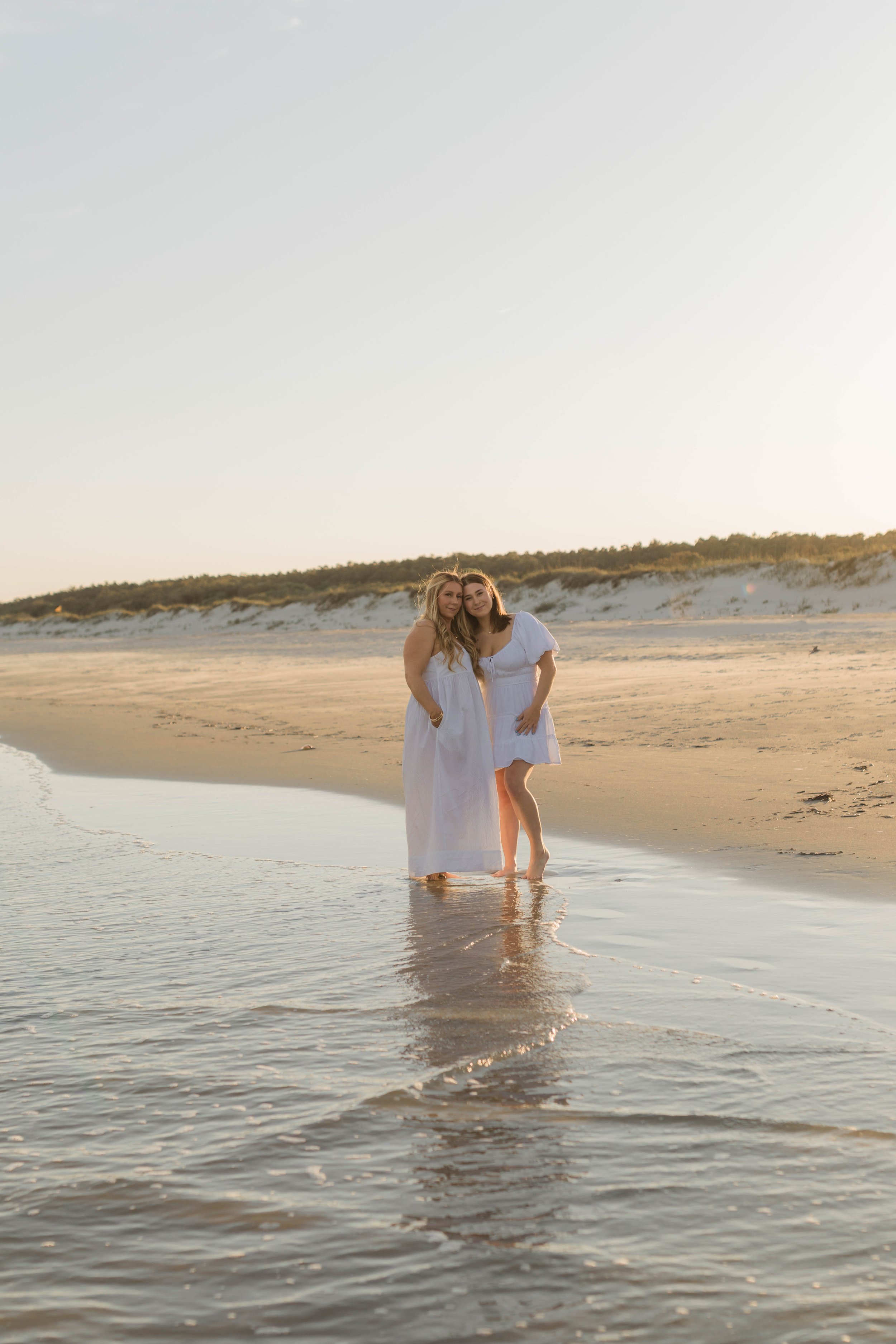 Mother and three daughters smiling and walking barefoot along the shoreline at sunset, Huntington Beach State Park