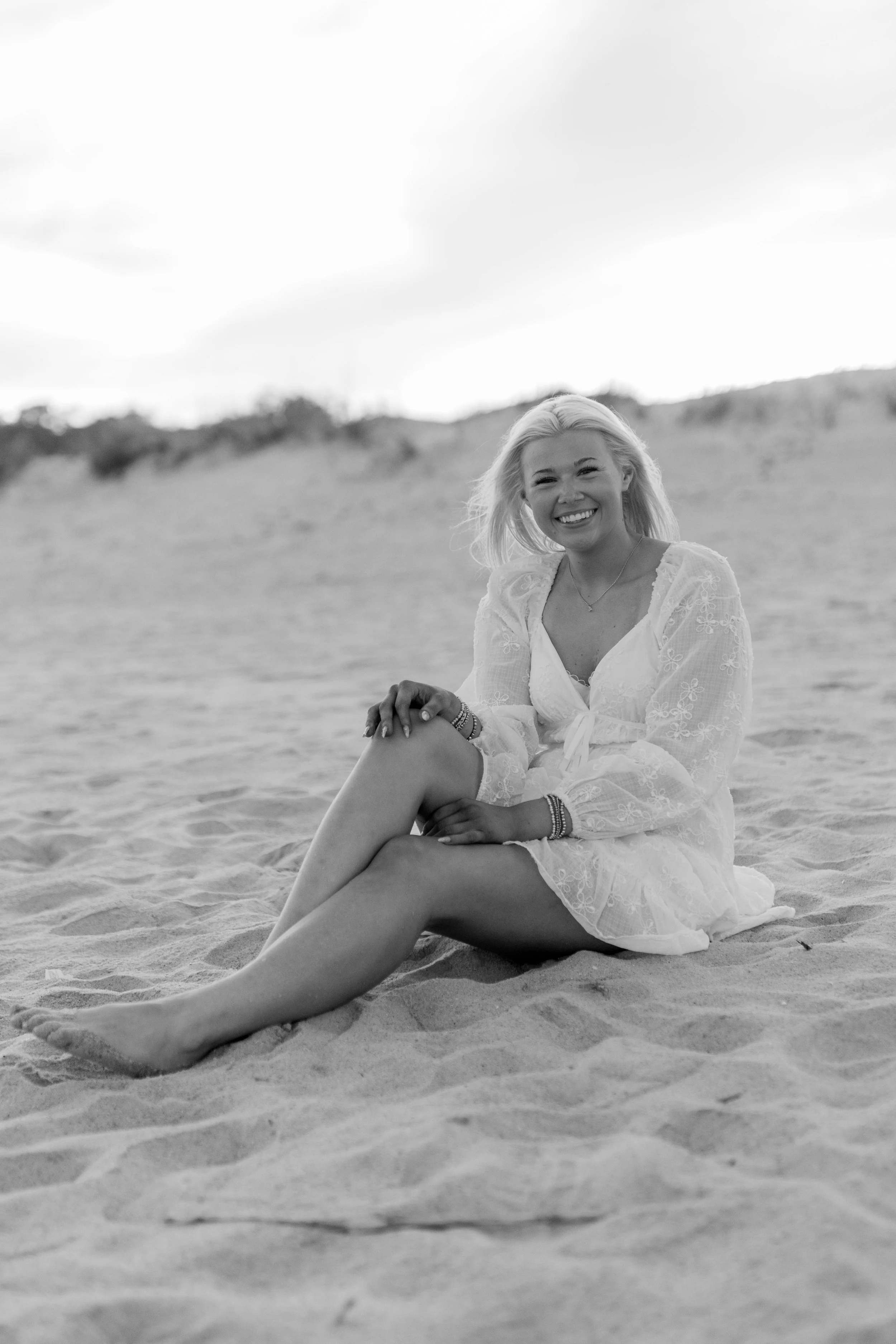 High school senior in Myrtle Beach wearing cap and gown during golden hour beach photo session, splashing in the water and smiling, taken by Myrtle Beach family and senior photographer.